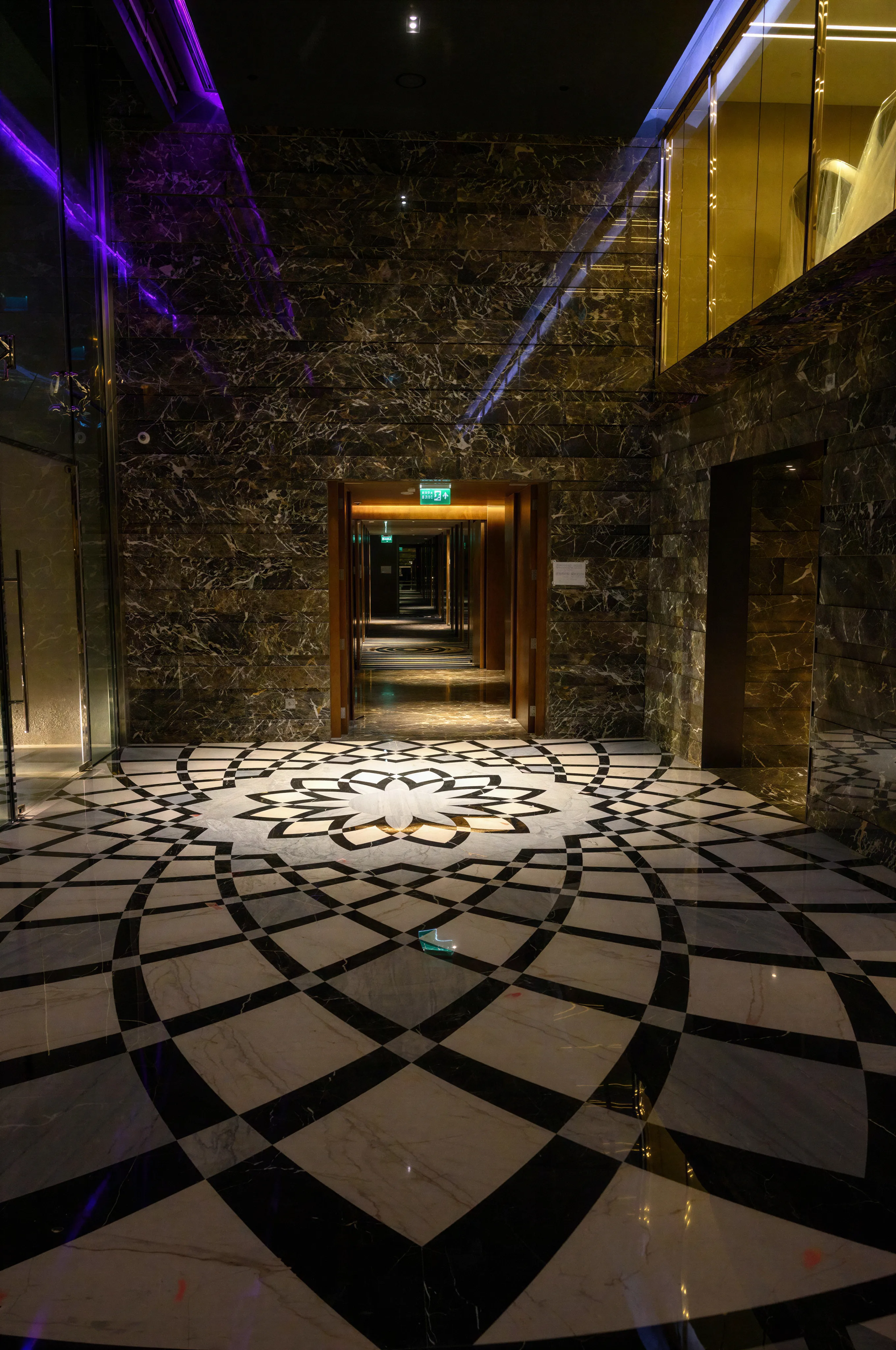 Hotel interior, highlighting custom natural stone medallion flooring, in black, white, and gray. Polished black marble and glass walls, and morphing RGB light.