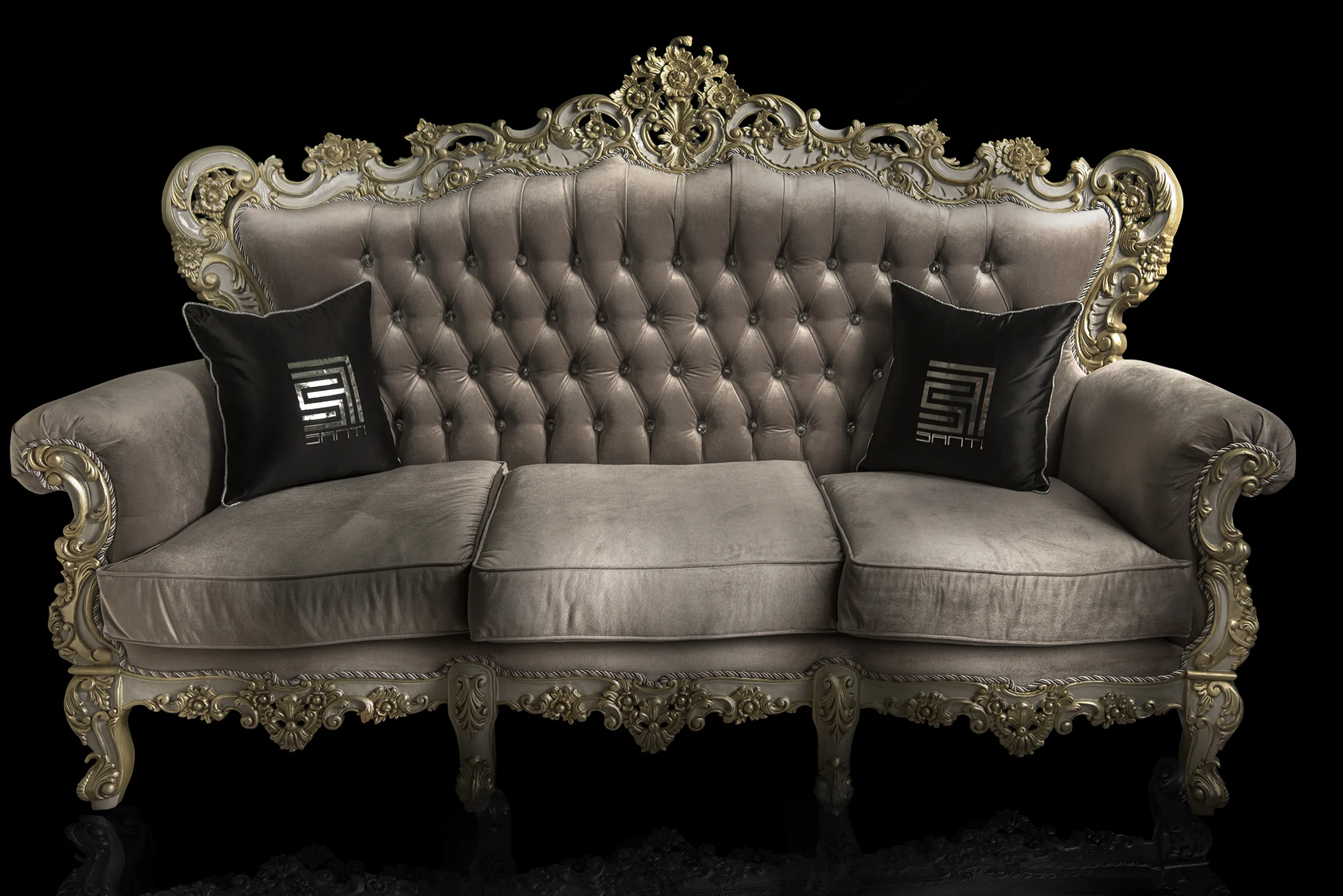 Front view of a hand-carved sofa, French modern fusion with gray Chesterfield padding and velvet fabric. Designer pillows sit at both ends and feature the designer's logo in reflective silver.