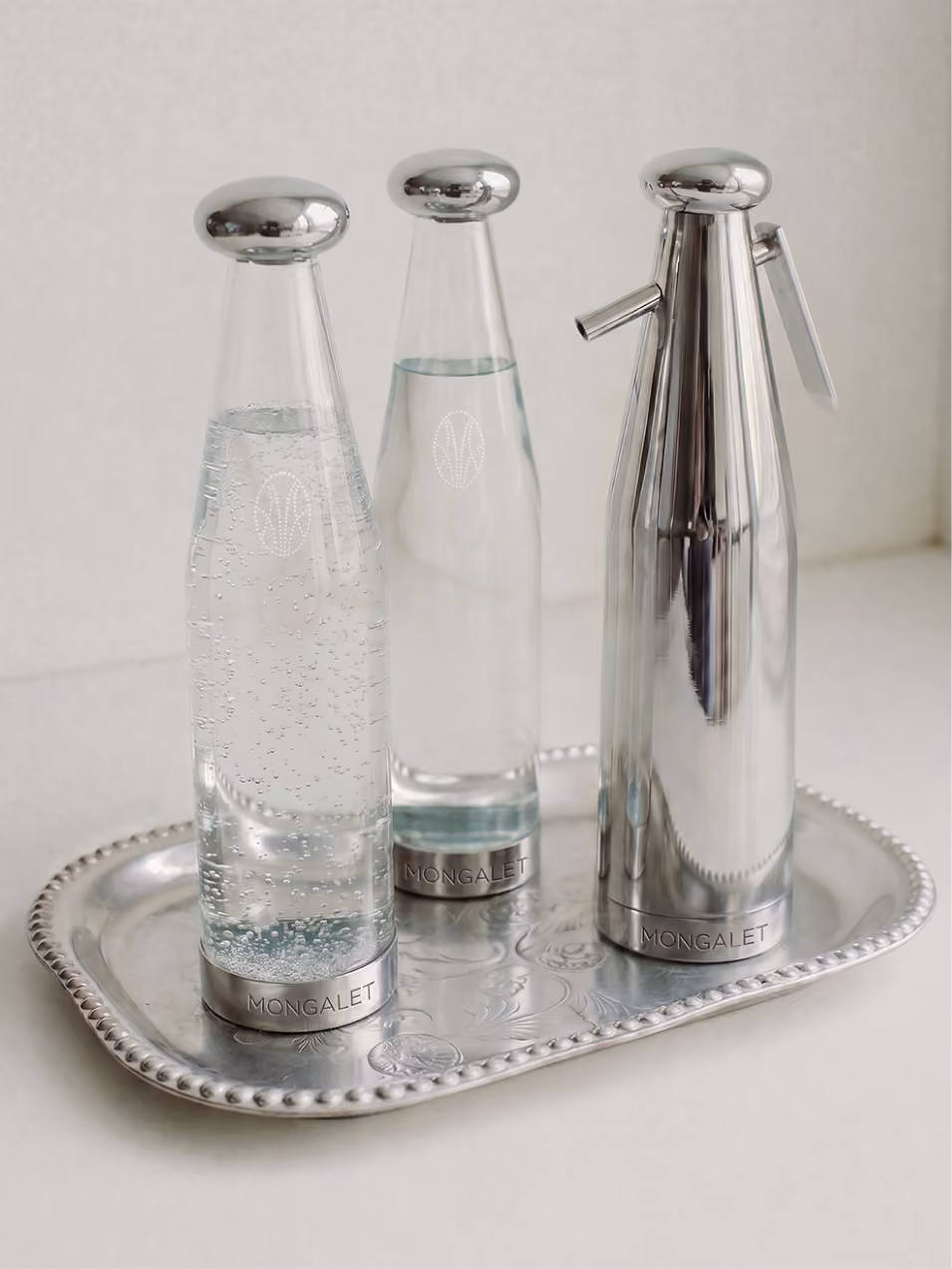 Deux bouteilles d’eau Mongalet et un siphon en métal sur un plateau ciselé