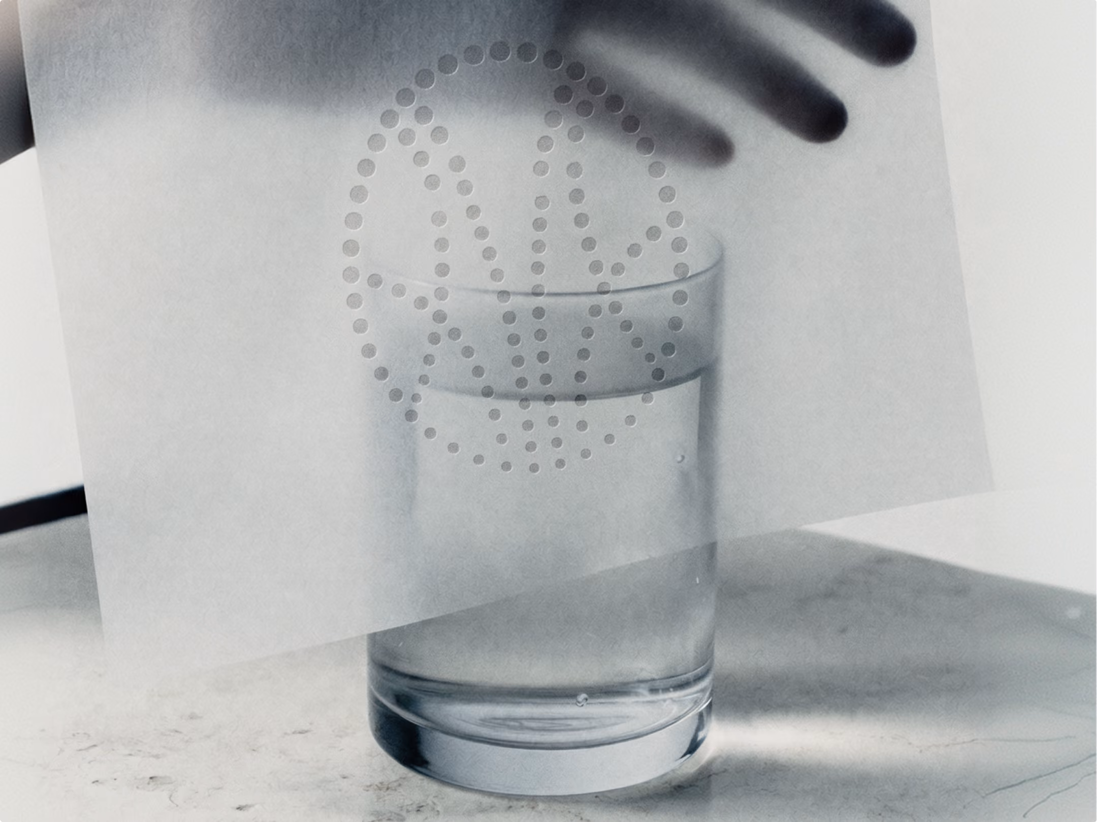 Main tenant une feuille translucide au logo Mongalet au-dessus d’un verre d’eau posé sur du marbre