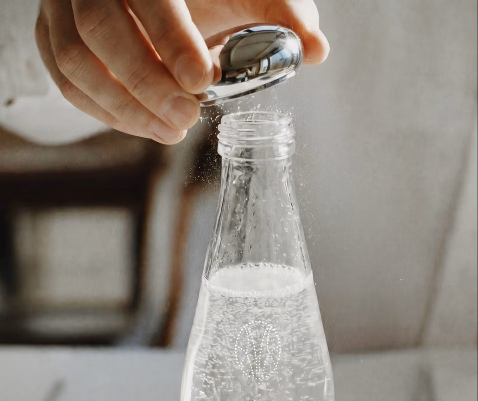Main ouvrant une bouteille en verre d’eau pétillante