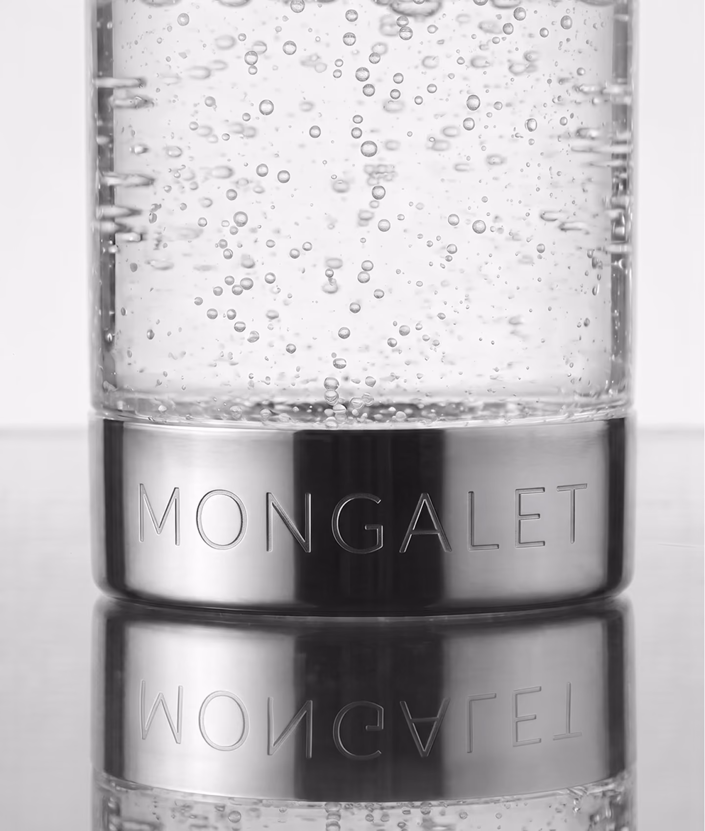 Verre d’eau pétillante Mongalet en noir et blanc avec bague métallique gravée et son reflet sur la table