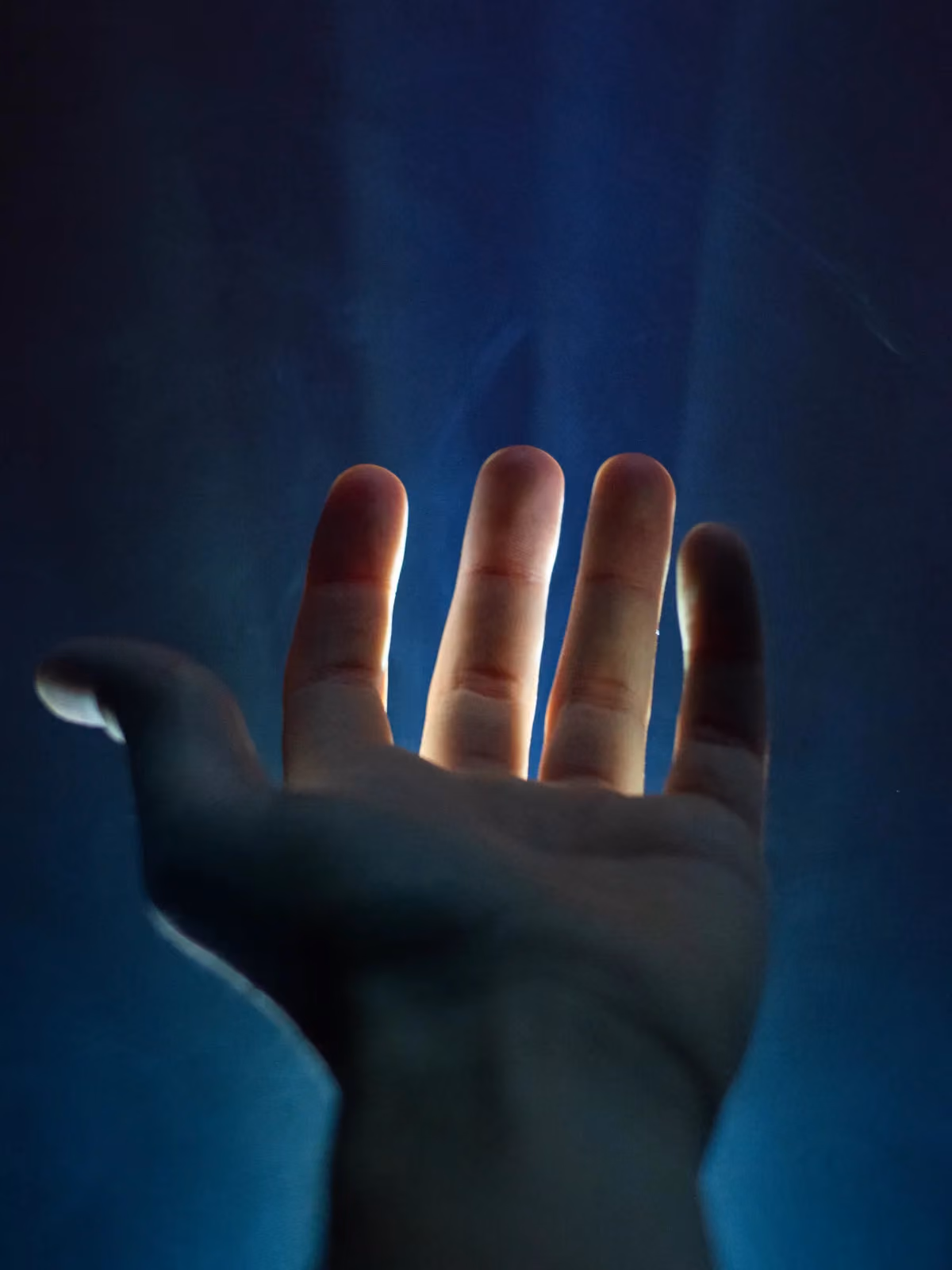 An open hand reaching towards softly lit blue fabric