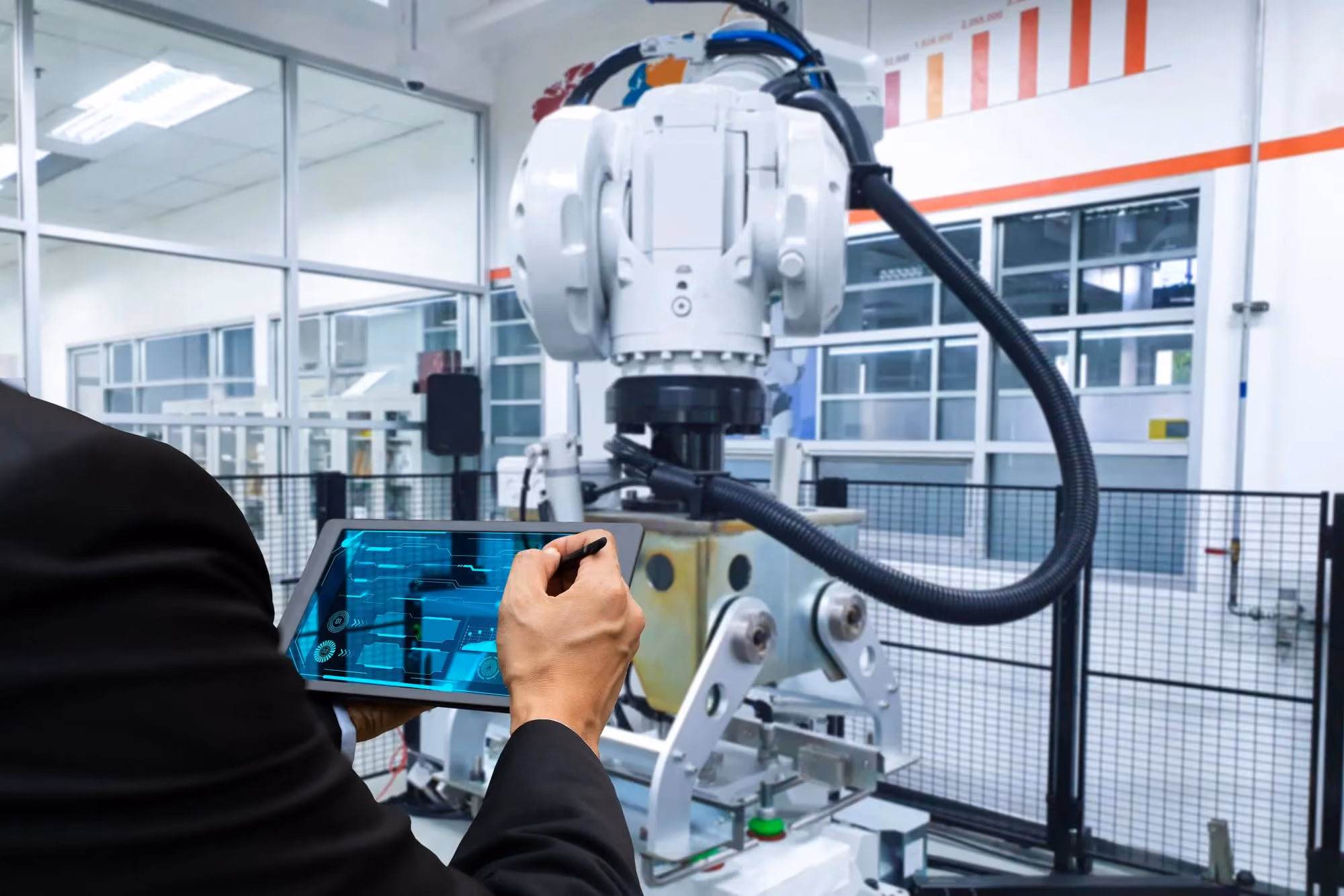 Engineer programming an industrial robot arm from a tablet on a factory floor
