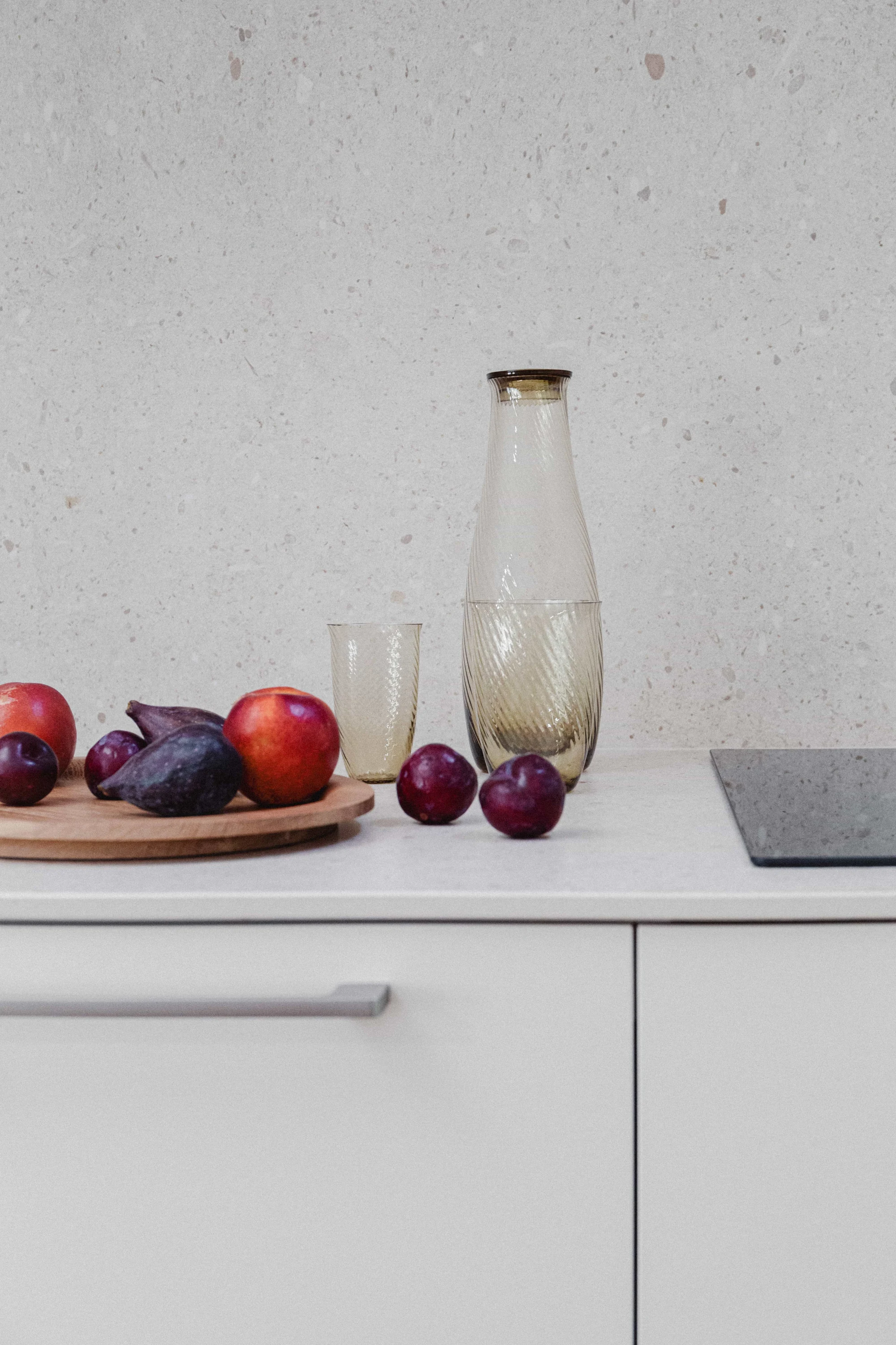 Encimera de cocina con frontal de terrazo con jarra y vaso de cristal ámbar, fruta y tabla de madera