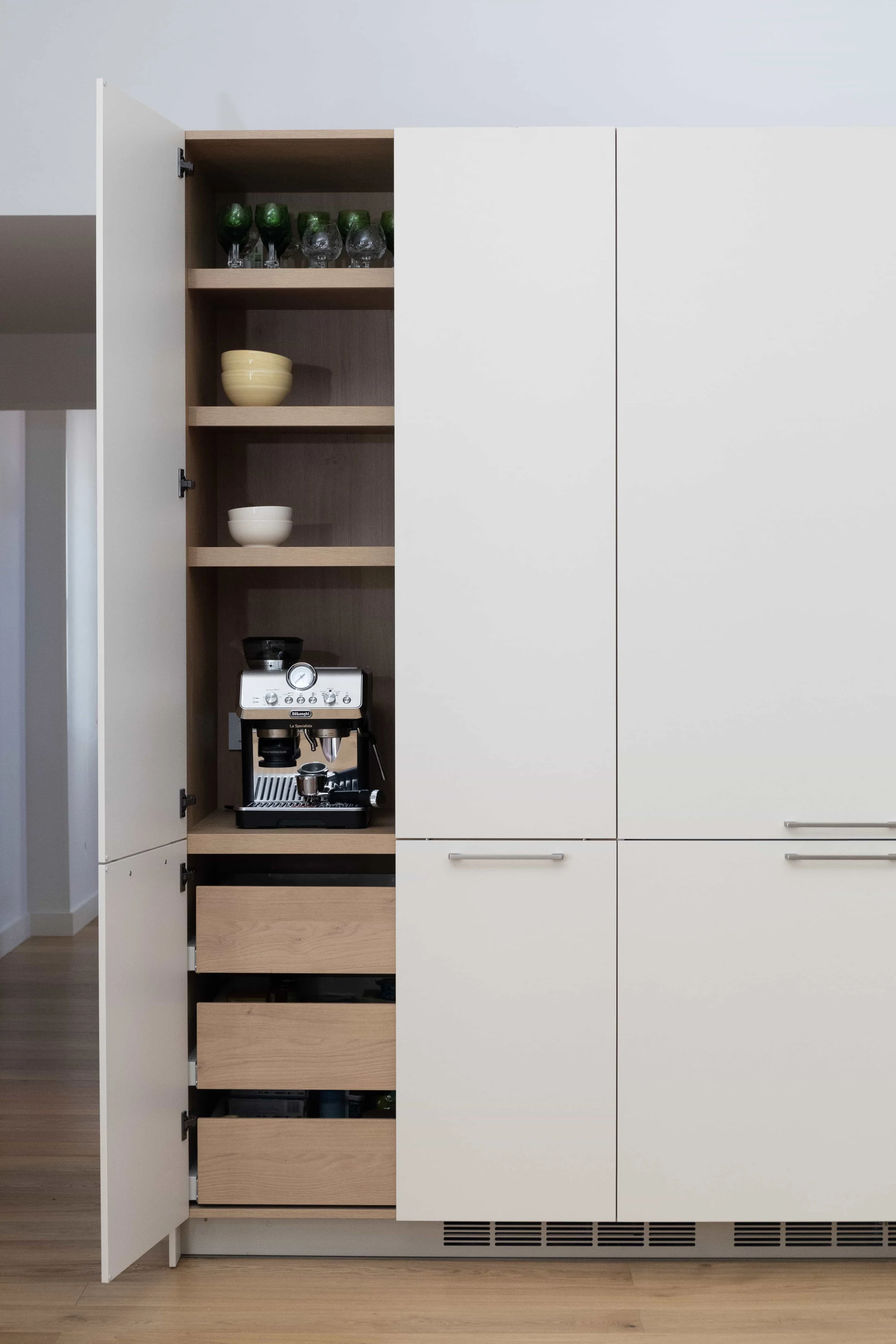 Armario alto de cocina moderno con puertas blancas e interior de madera que funciona como estación de café integrada.