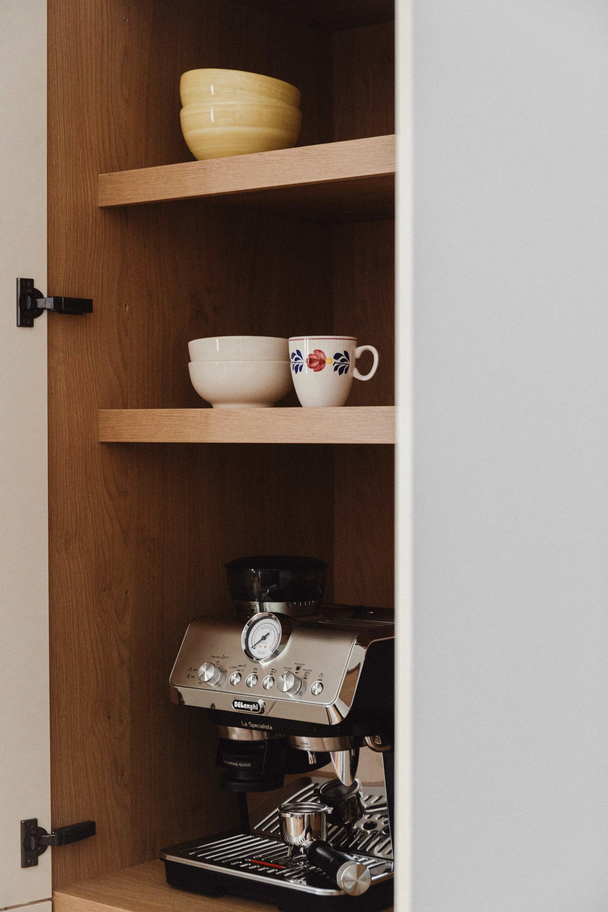 Interior de armario de cocina en madera con cafetera y vajilla.