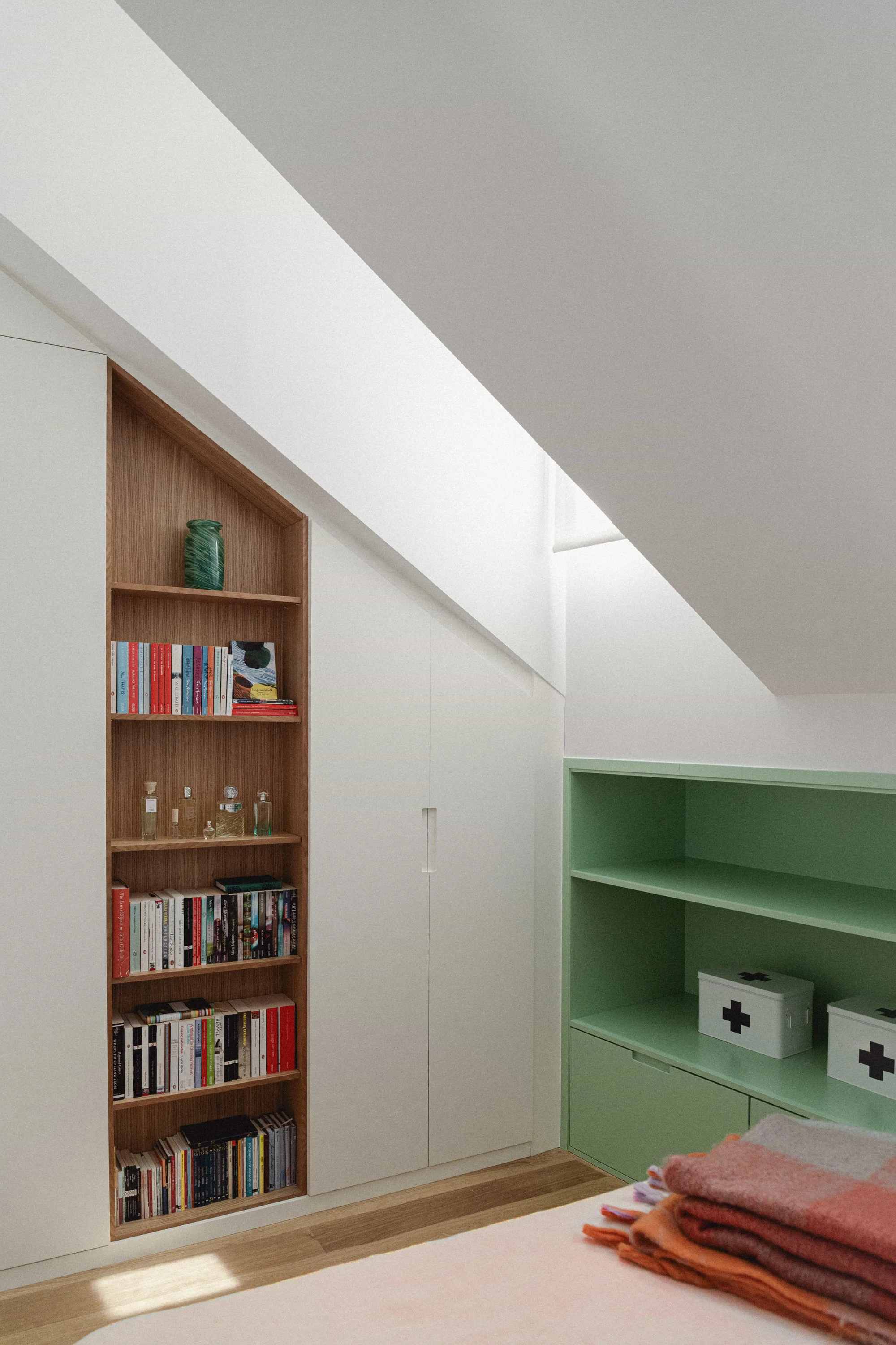 Dormitorio abuhardillado con estantería de madera empotrada, armario blanco a medida y estantería verde.