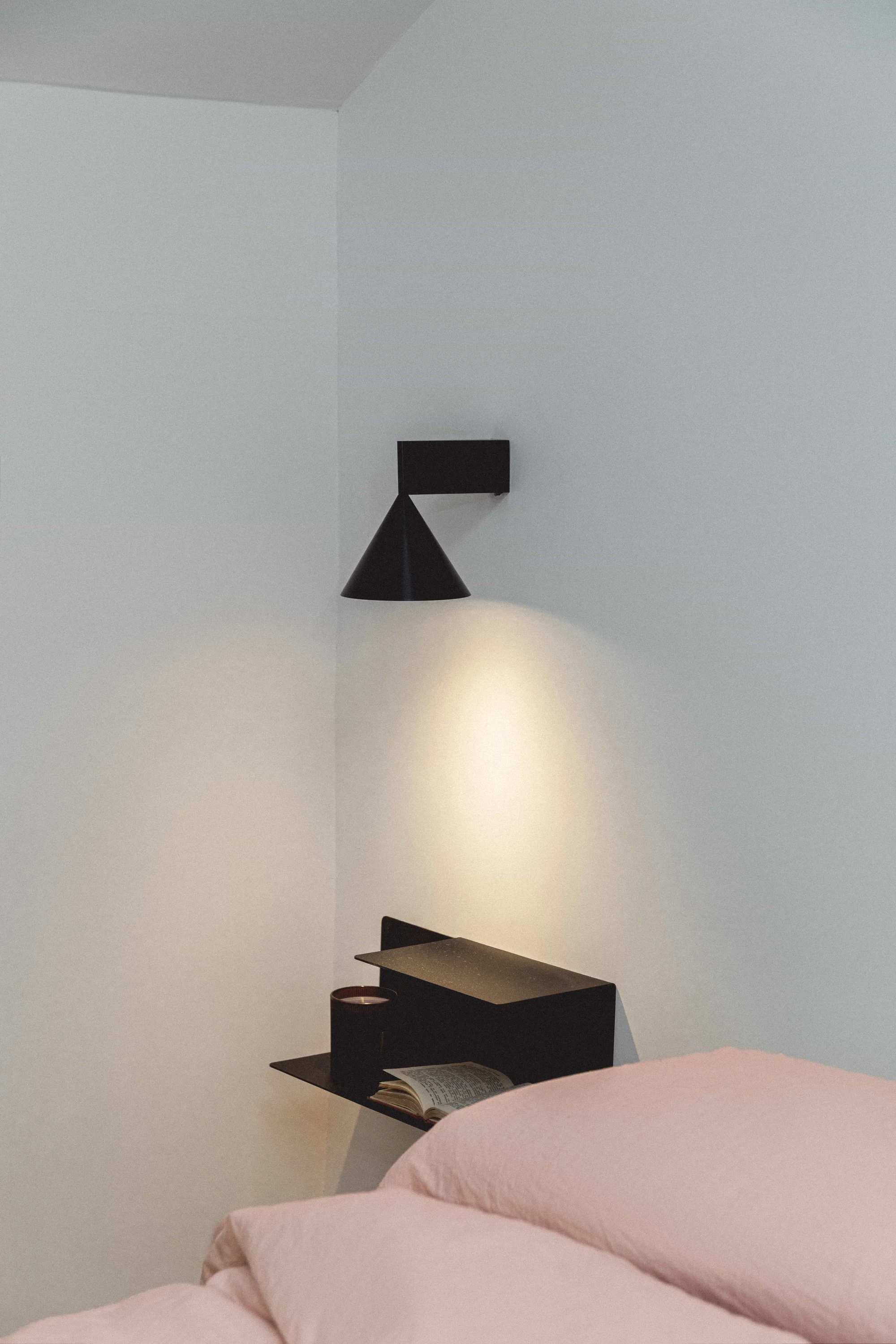 Dormitorio minimalista con aplique de pared y mesita de noche flotante.