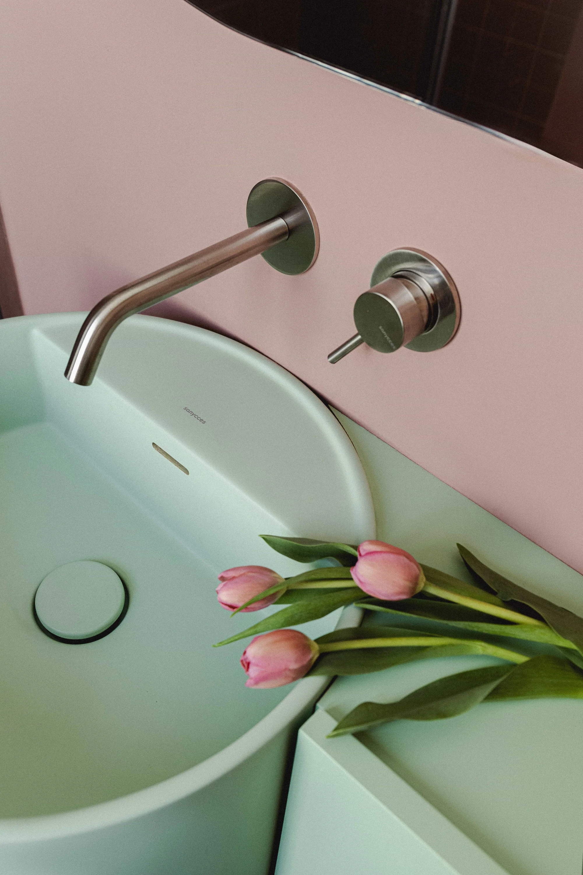 Lavabo baño estilo retro de color verde menta y pared rosa.