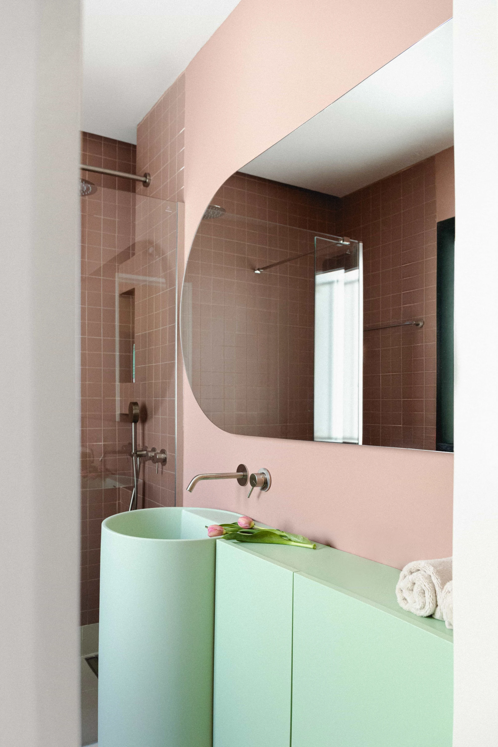 Baño estilo retro con pared de azulejos rosa, lavabo cilíndrico y mueble verde menta.