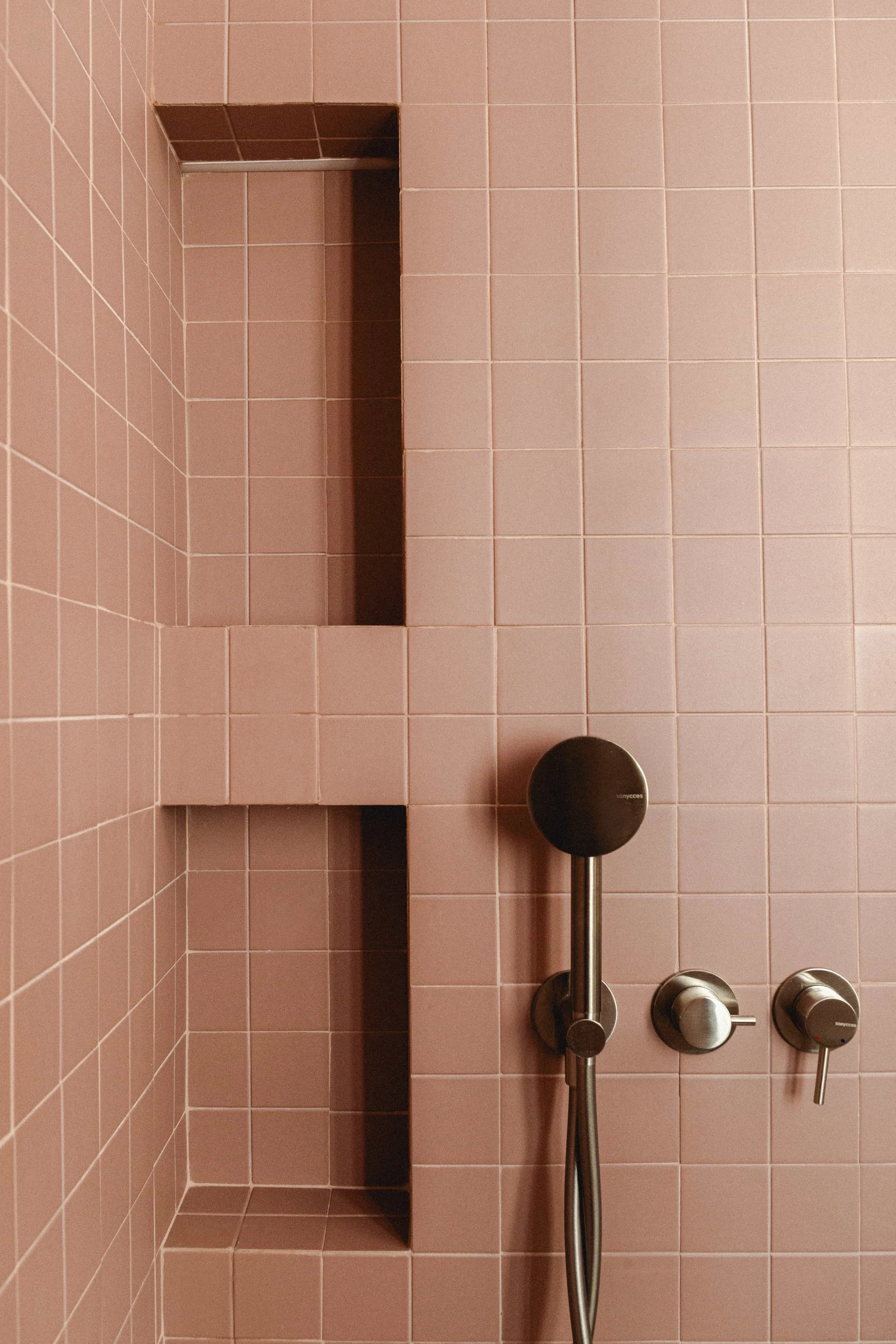 Ducha con azulejos rosa, hornacinas de obra y grifería en acabado acero.