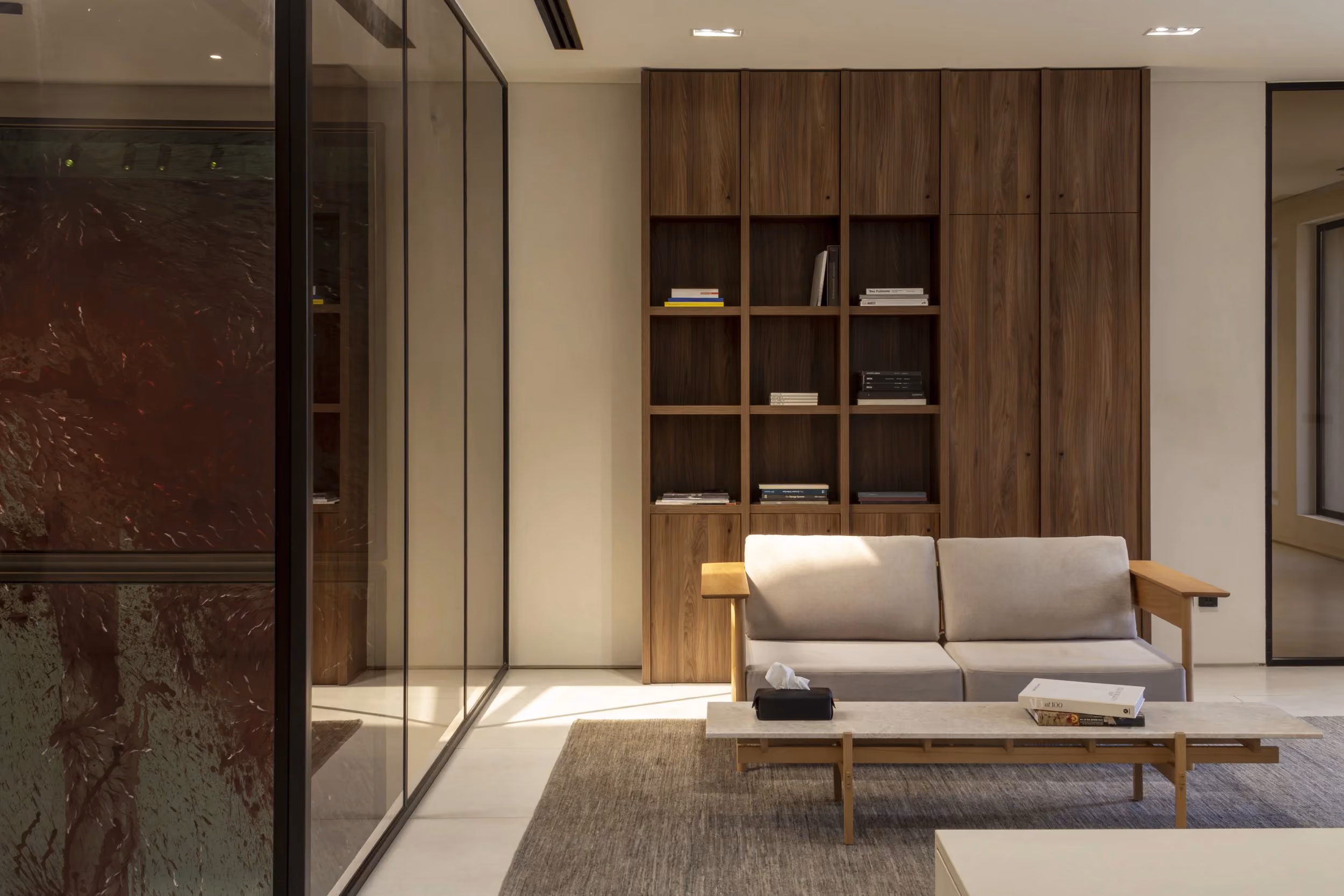 Modern living room with beige sofa, wooden coffee table, gray rug, and tall wooden bookshelf.