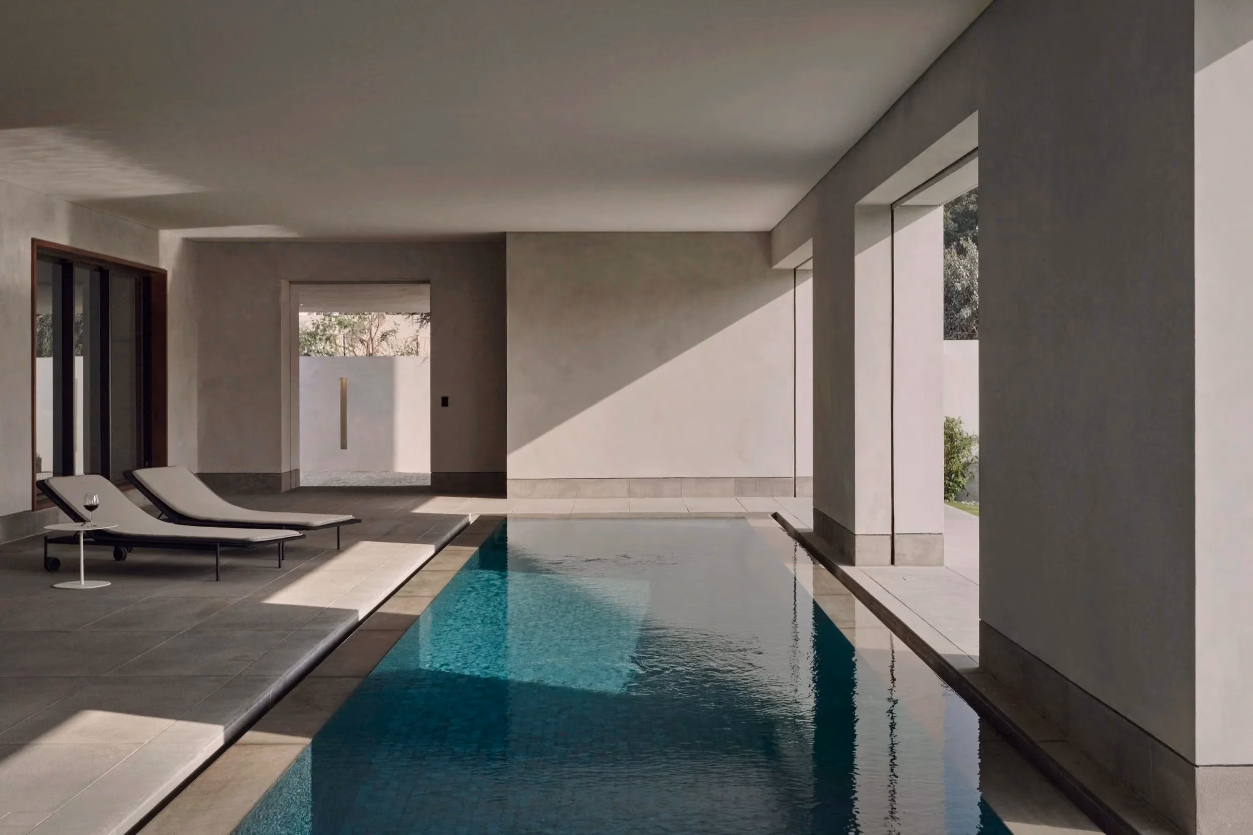 Minimalist covered indoor pool area with two lounge chairs and small side table with wine glass.