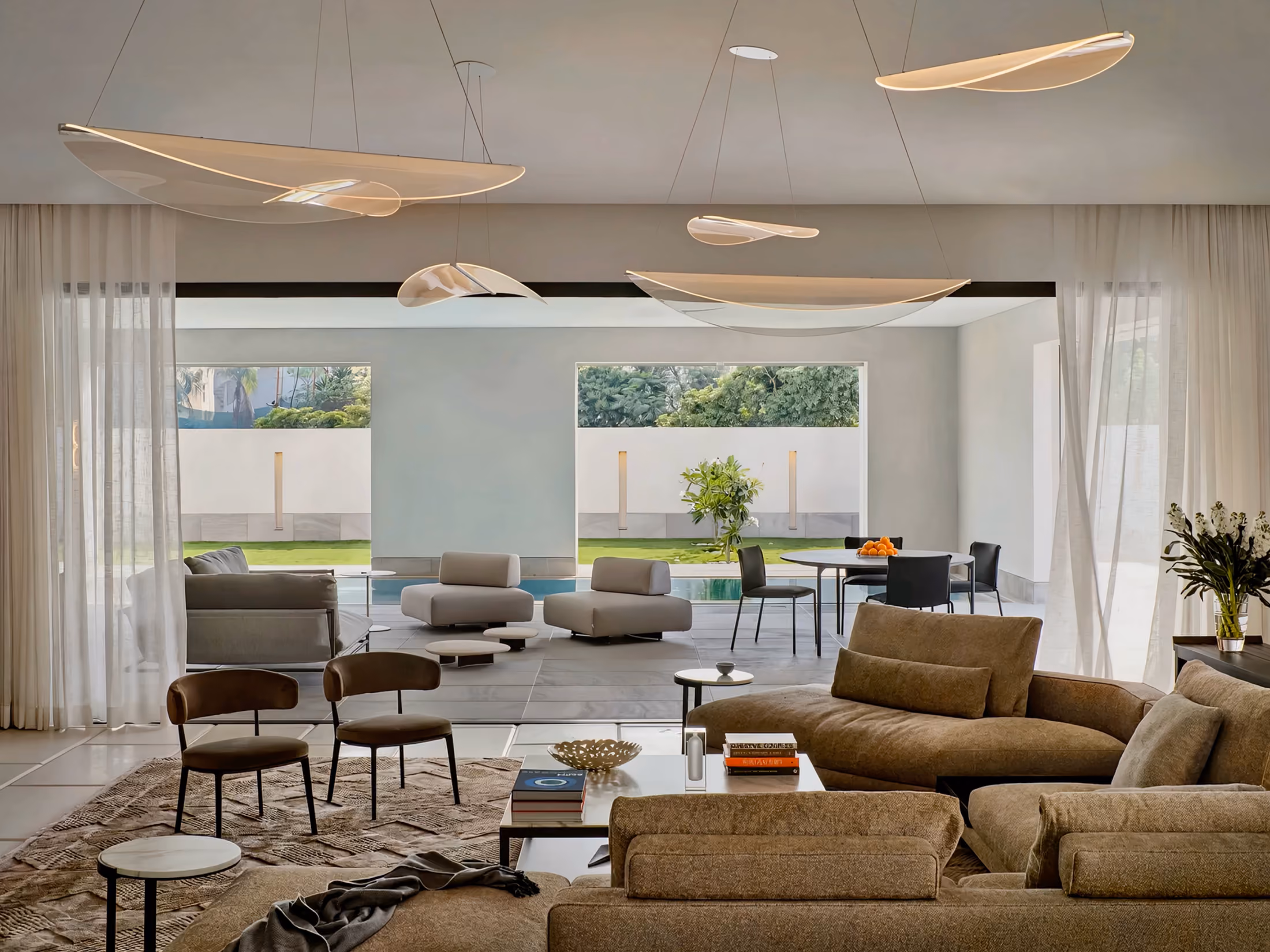 Modern living room with beige sofas, two chairs, and large windows looking onto a patio and garden.