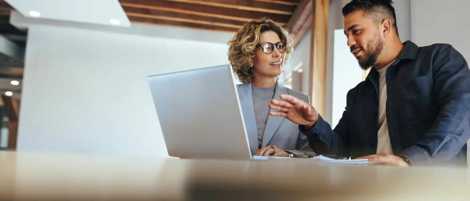 Recruiter and client talking over a laptop in a modern office with exposed wood beams