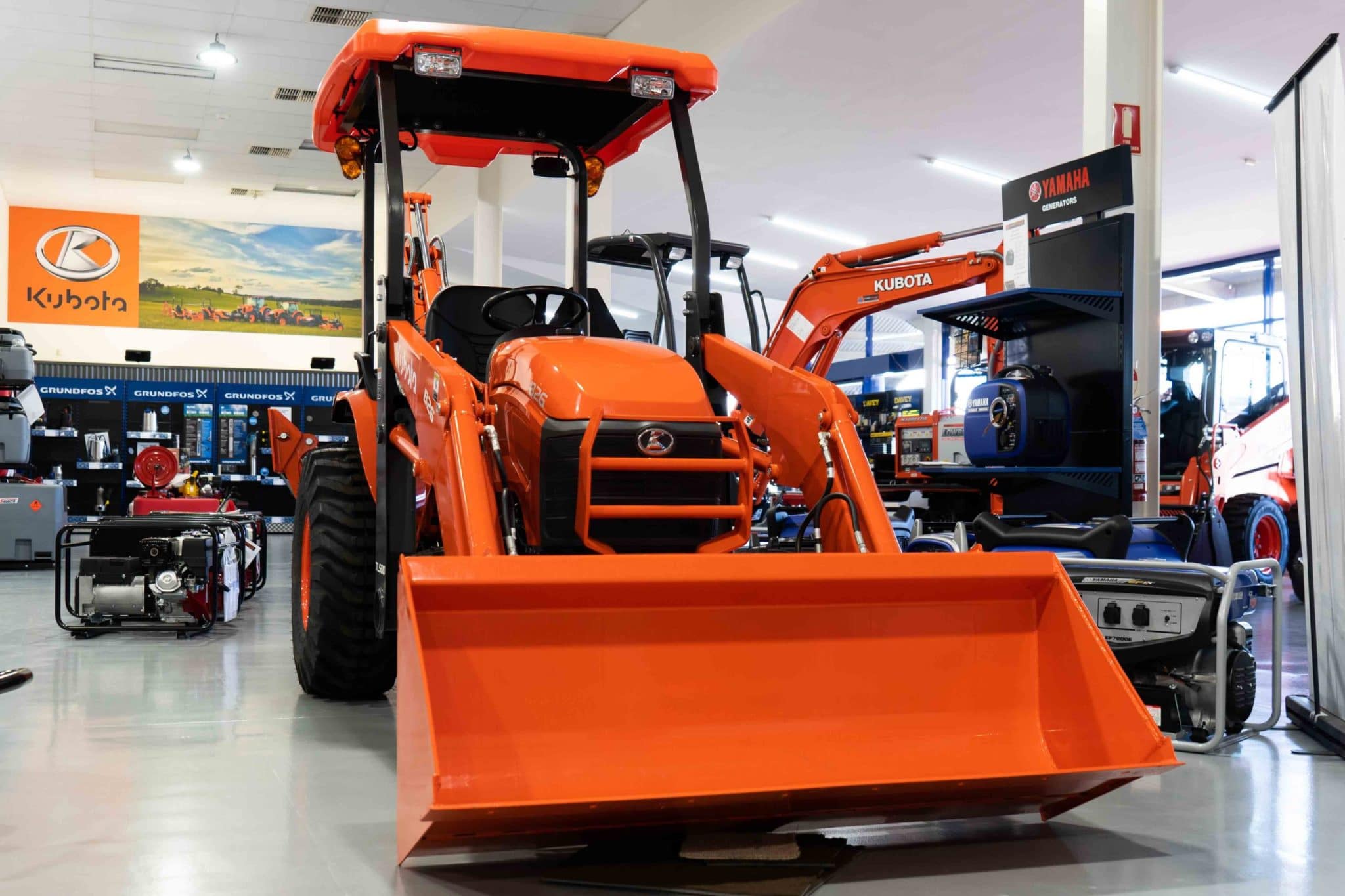 Orange Kubota front loader tractor inside a showroom with other equipment and generators.