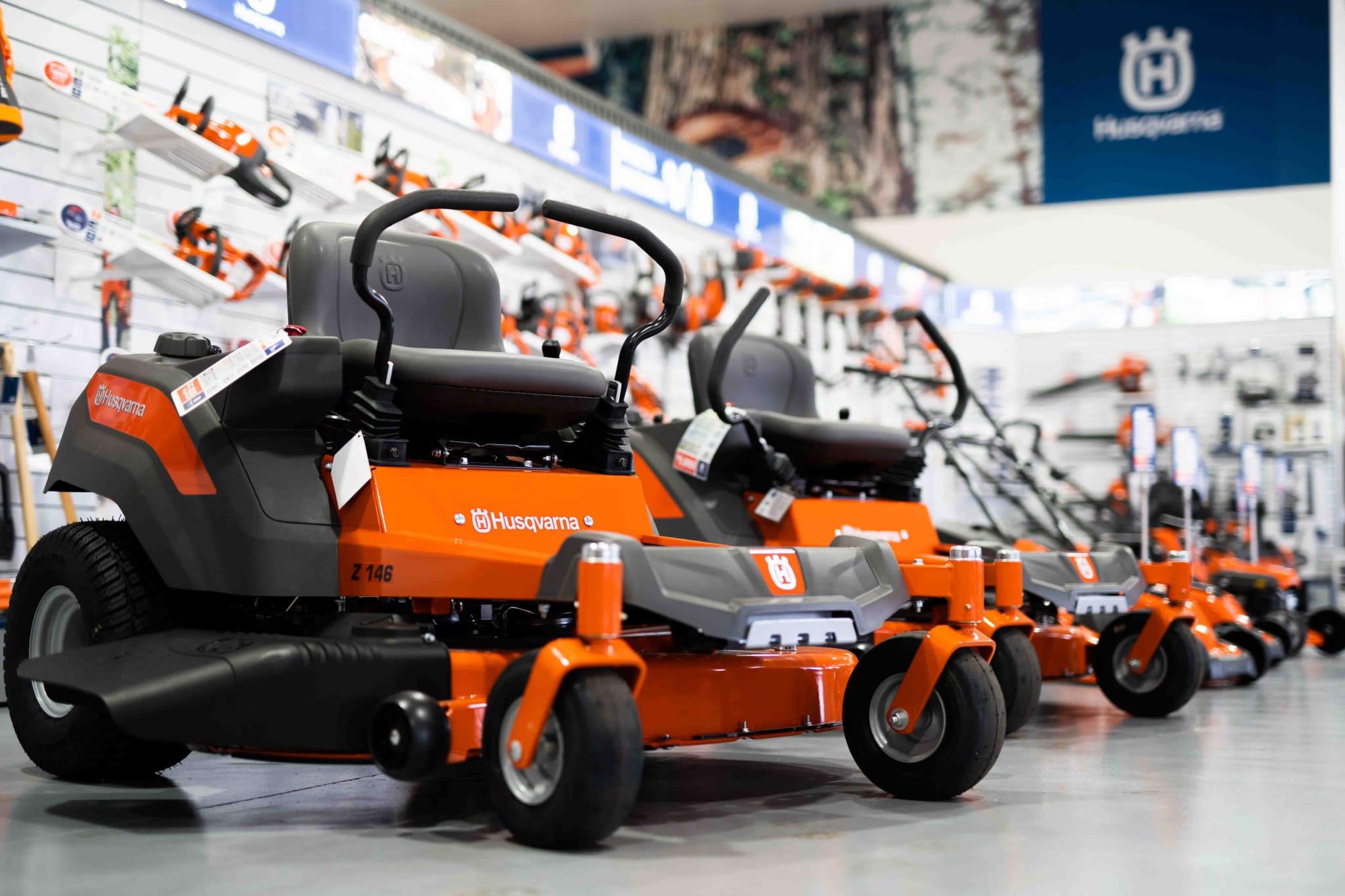 Row of orange Husqvarna riding lawn mowers displayed in a store with gardening tools on the walls.