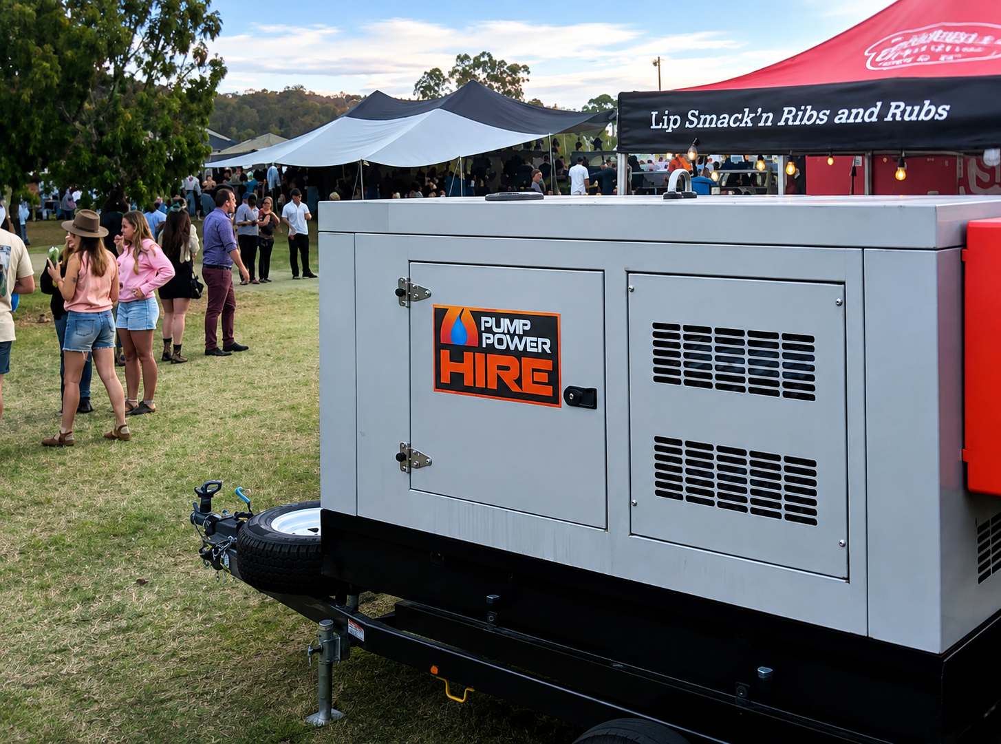 Large power generator with Pump Power Hire logo at an outdoor event with people and food stalls.