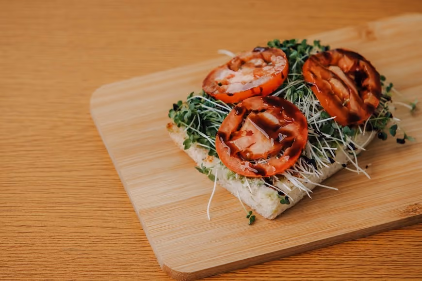 Open-faced sandwich with alfalfa sprouts, microgreens, grilled tomato slices, and balsamic glaze on bread.