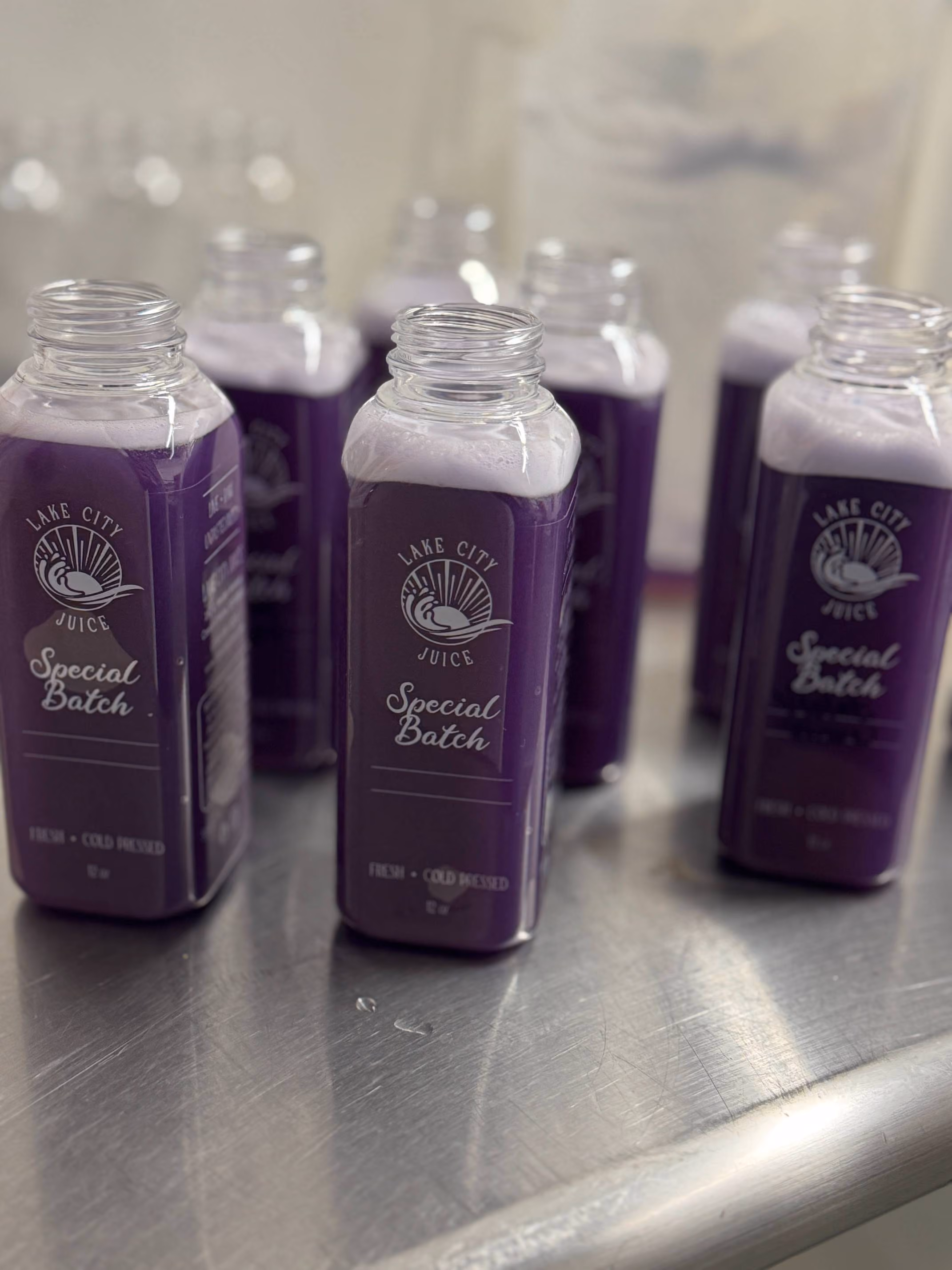Multiple bottles of purple juice labeled Lake City Juice Special Batch on a metal surface.