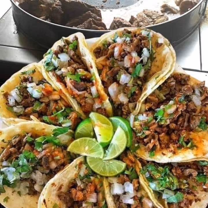 Plate with several tacos filled with meat, onion, cilantro, and lime wedges in the center.