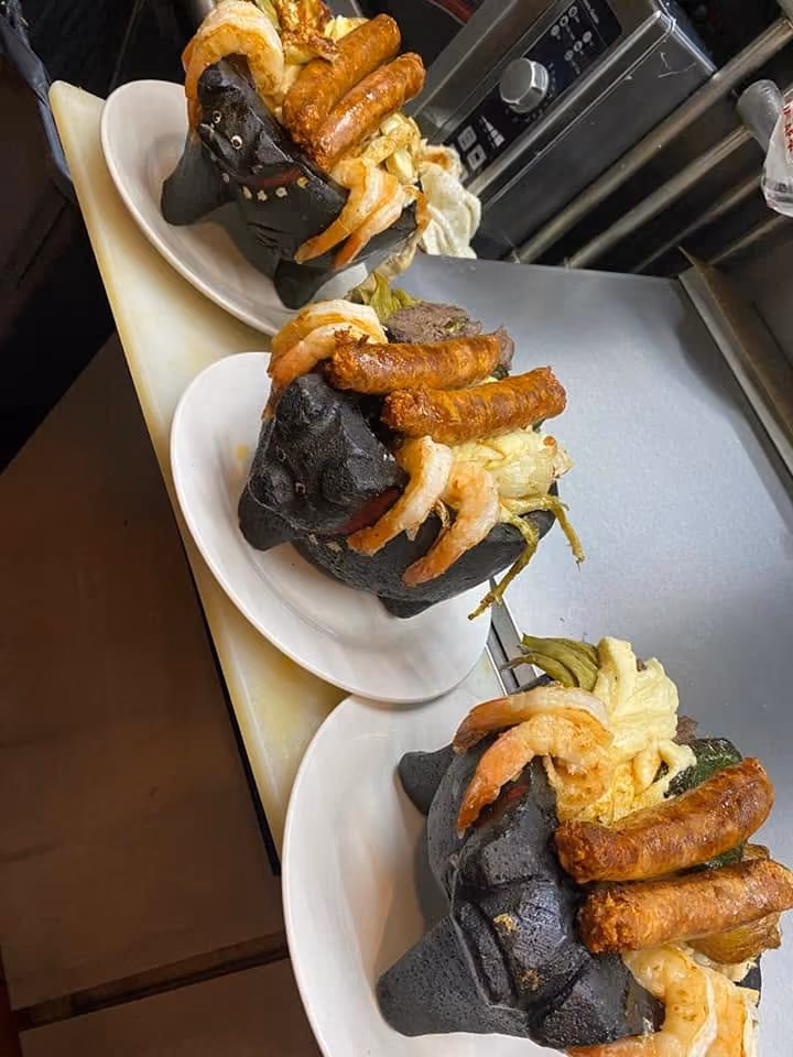 Three plates each holding a black molcajete filled with shrimp, sausages, cheese, and vegetables.