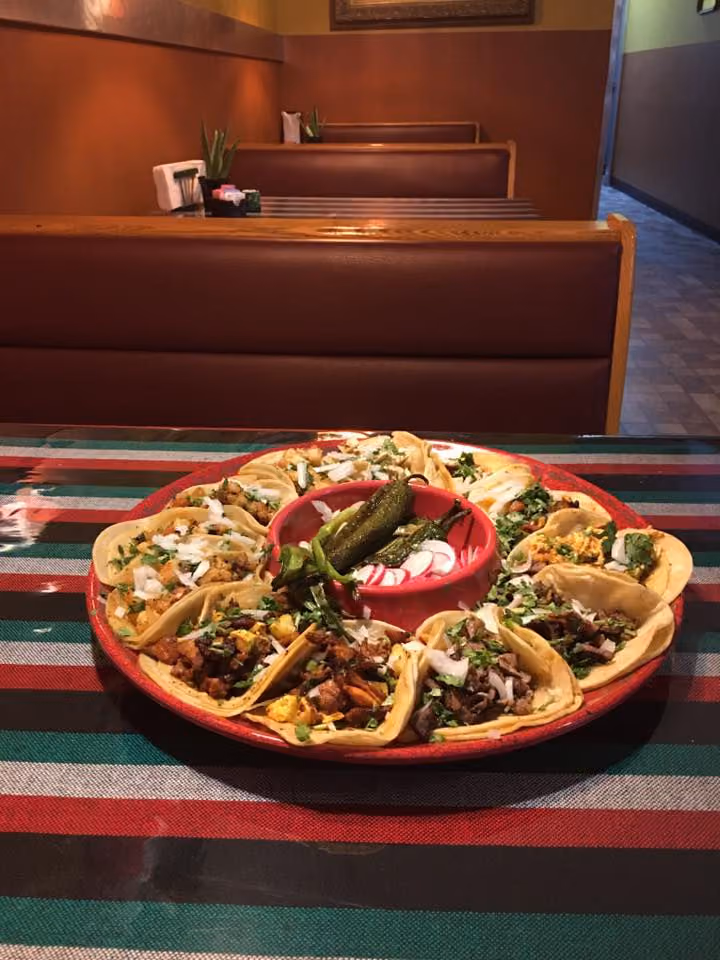 Plate of assorted tacos arranged in a circle with grilled peppers and sliced radishes in the center.