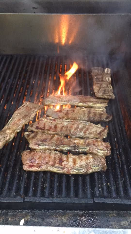 Several pieces of ribs grilling over open flames on a barbecue grill.