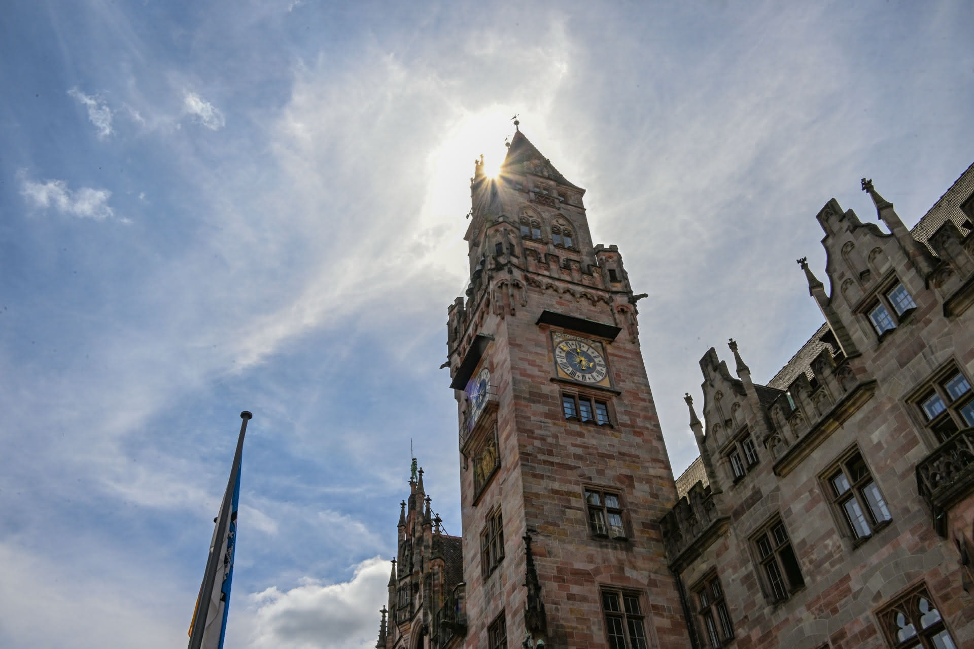 Historischer Uhrturm eines steinernen Rathauses mit Sonne, die hinter dem Turm scheint.