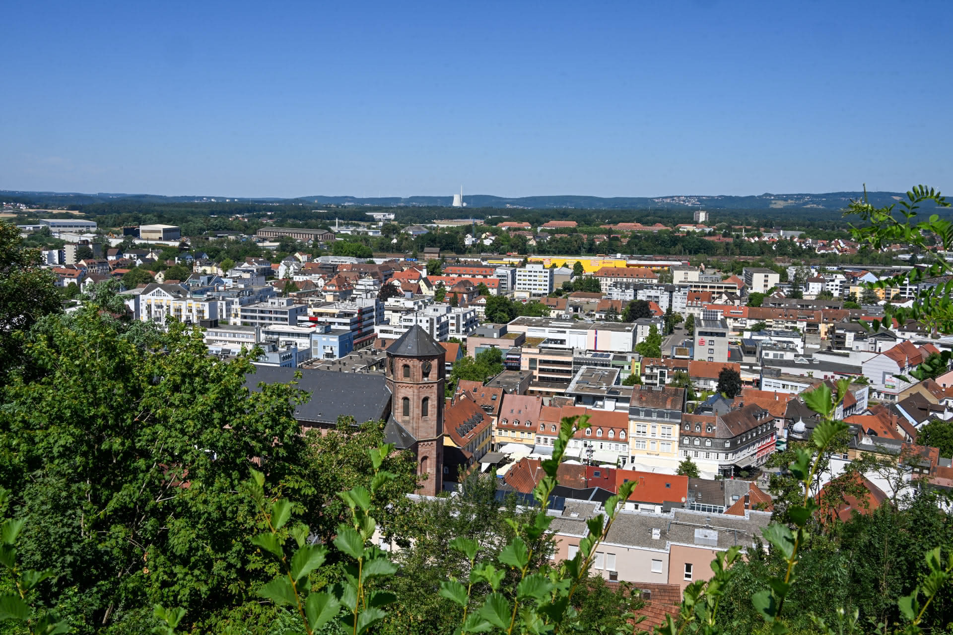 Panorama der Stadt Homburg mit Kirche und Infrastruktur, umgeben von grünen Bäumen unter blauem Himmel.