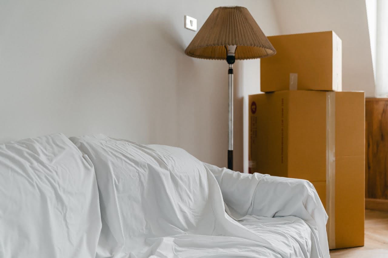 Weiß bezogenes Sofa neben Stehlampe und gestapelten Umzugskartons in einem Raum.