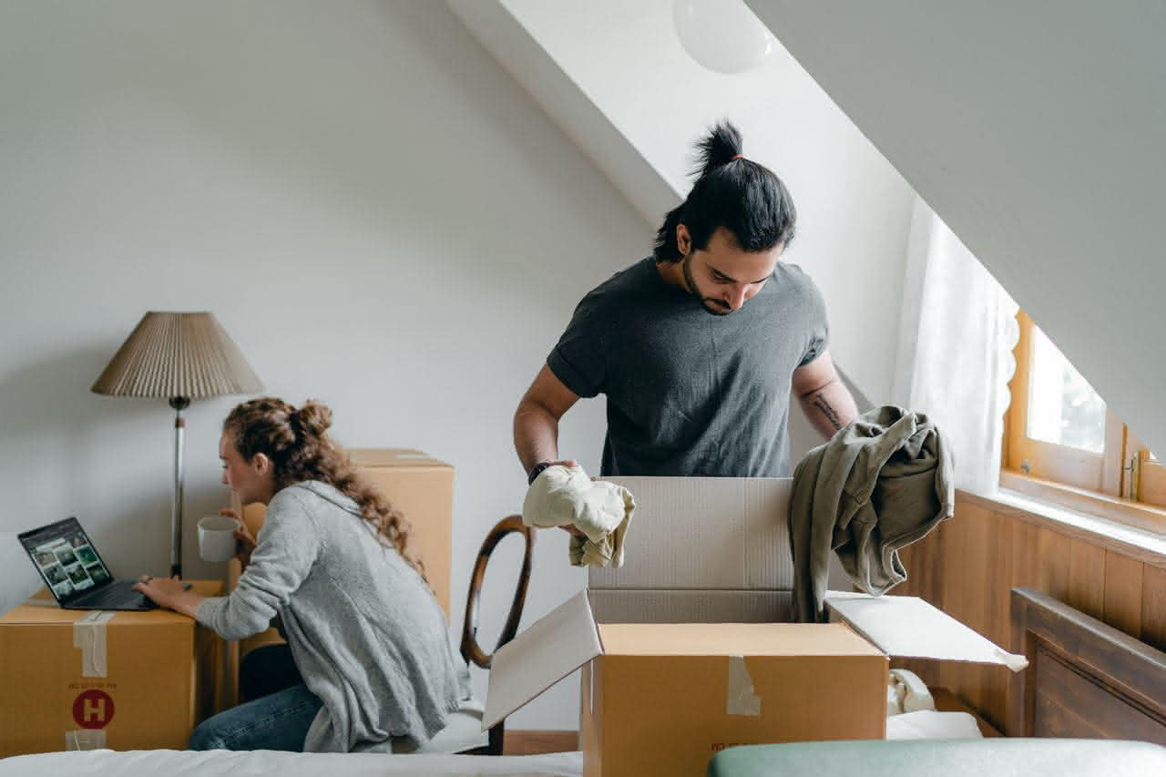 Junges Paar packt Kartons in hell beleuchtetem Zimmer während eines Umzugs.