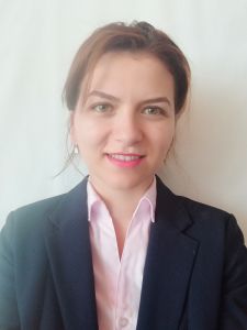 Porträt einer lächelnden Frau in einem schwarzen Blazer und rosa Hemd vor einem weißen Hintergrund.