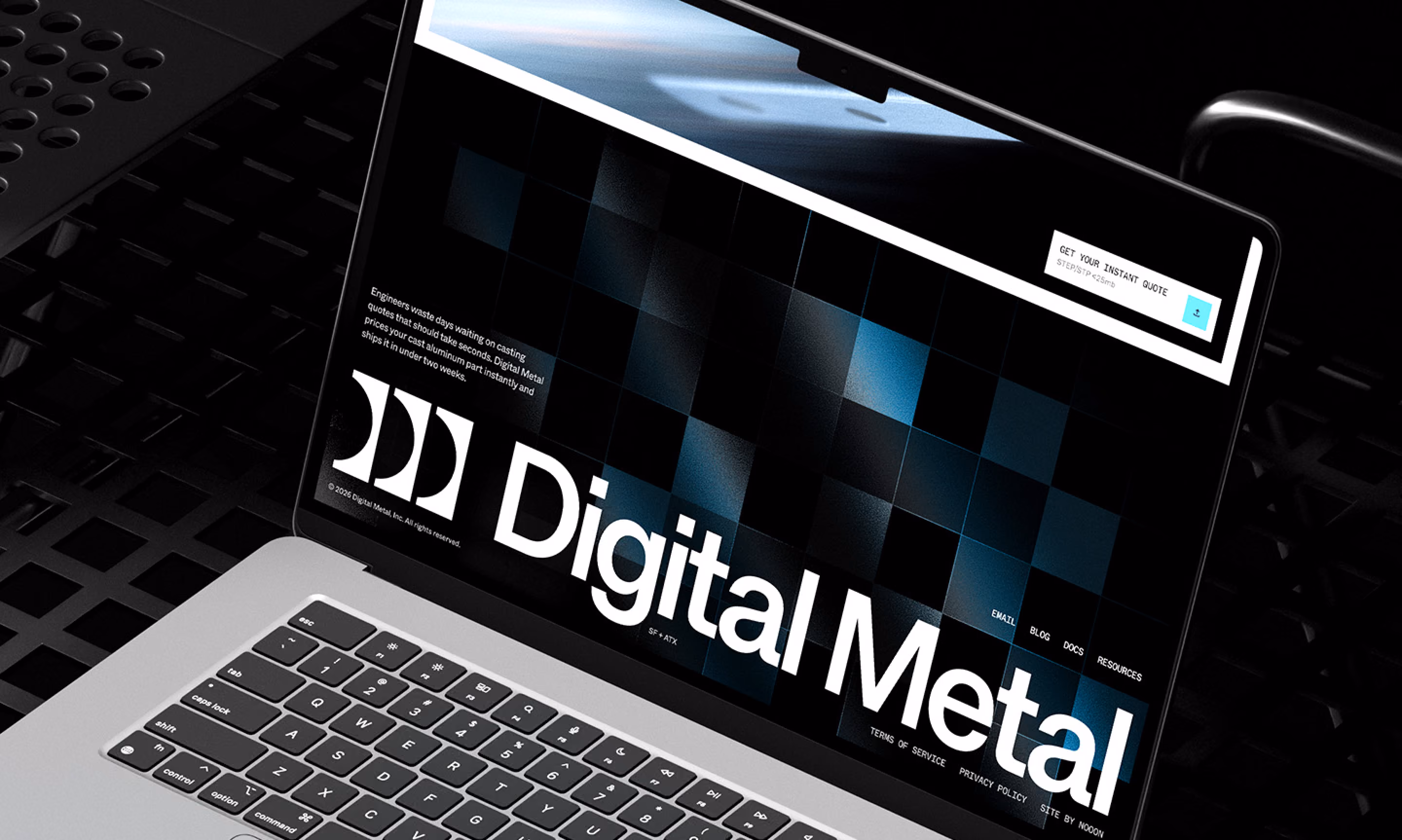 Laptop showing the Digital Metal homepage with a large wordmark over a dark checkered hero image.
