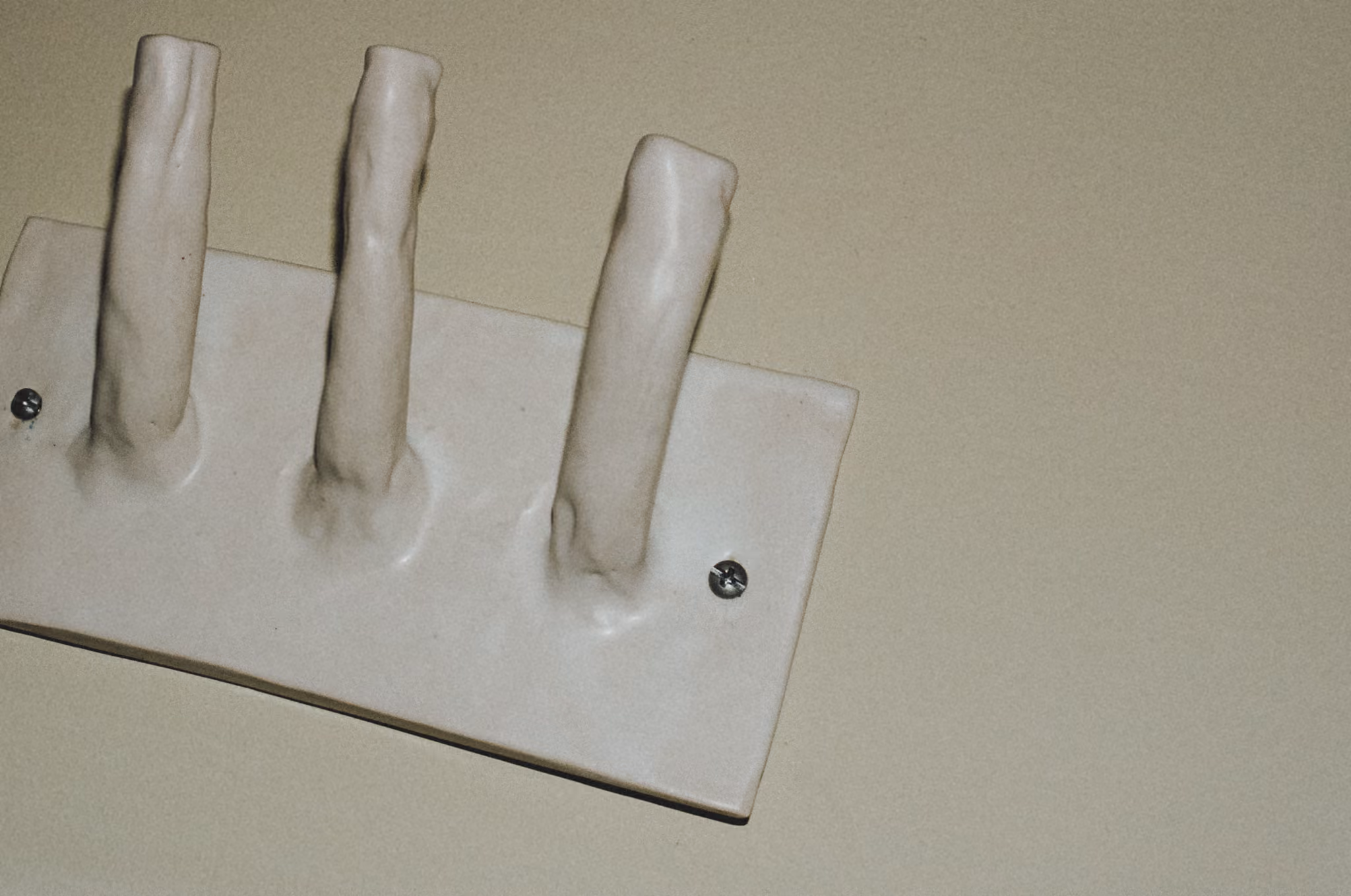White ceramic wall hook rack with three rounded hooks mounted on a beige wall.
