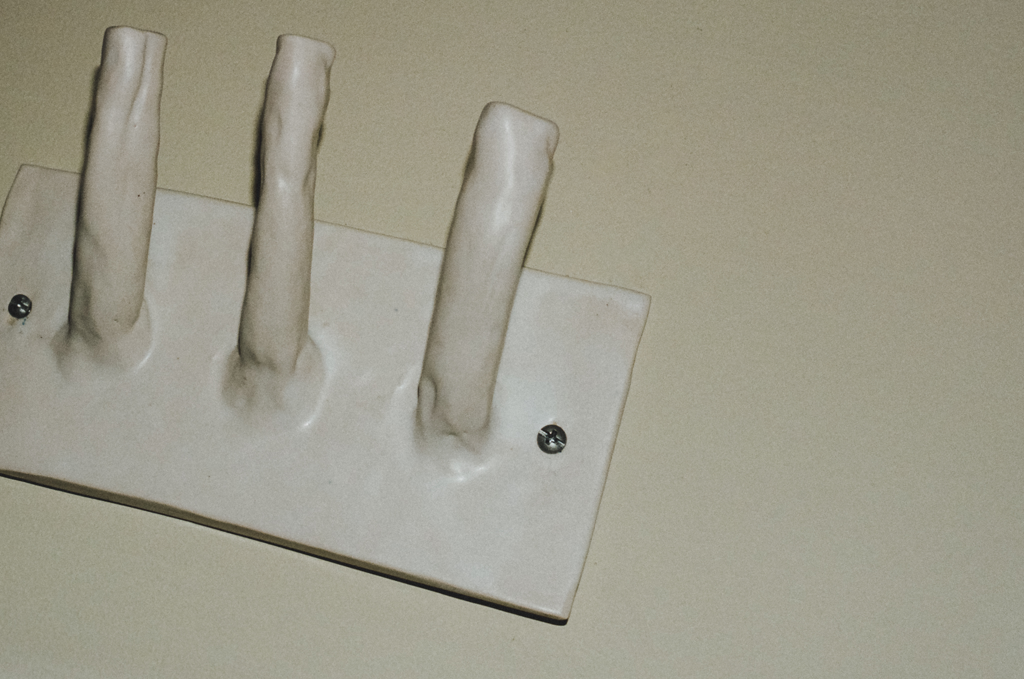 White ceramic wall hook rack with three rounded hooks mounted on a beige wall.