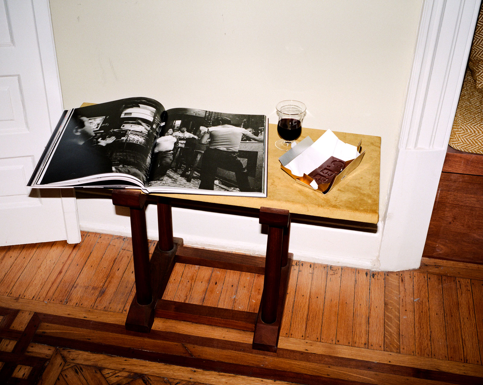 Small table with an open black-and-white photo book, chocolate bar, and a glass of red wine.