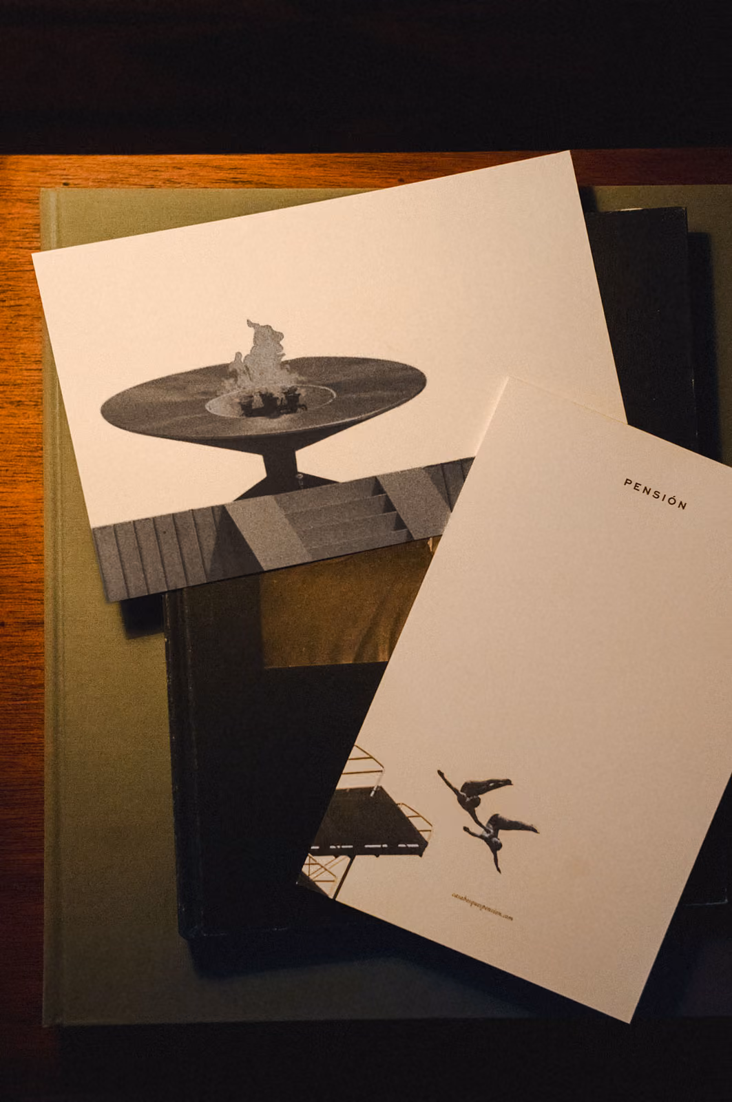 Two postcards on books: one with a flame sculpture, the other with two divers and text PENSIÓN.