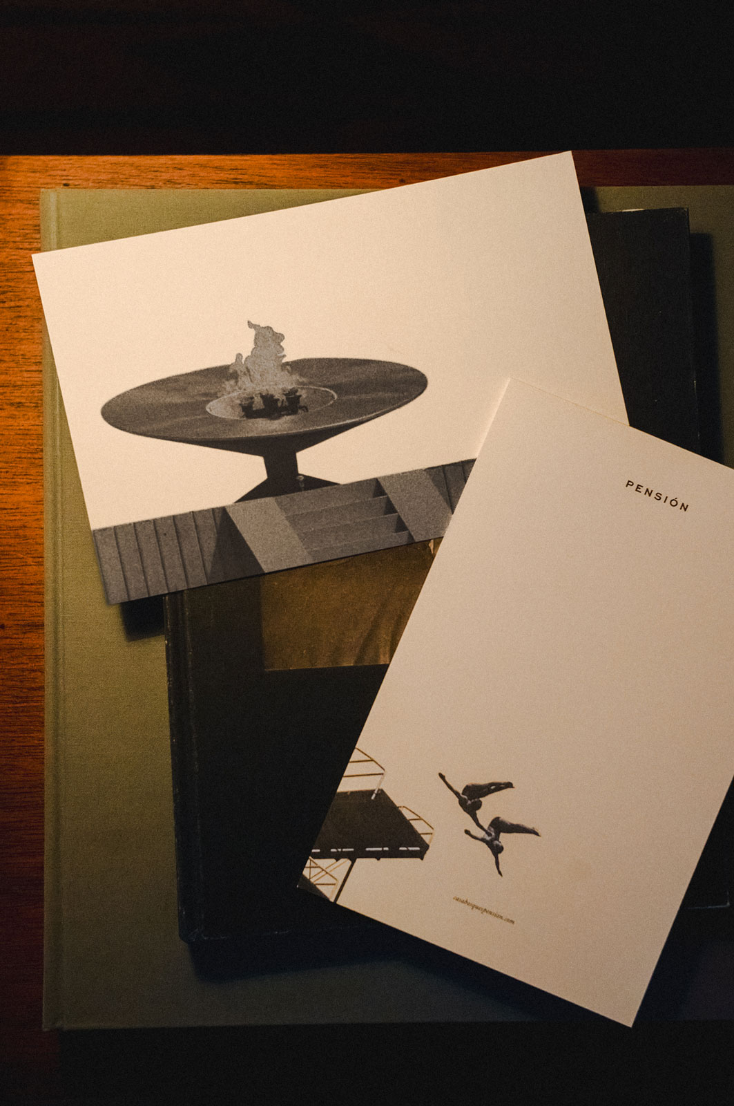 Two postcards on books: one with a flame sculpture, the other with two divers and text PENSIÓN.