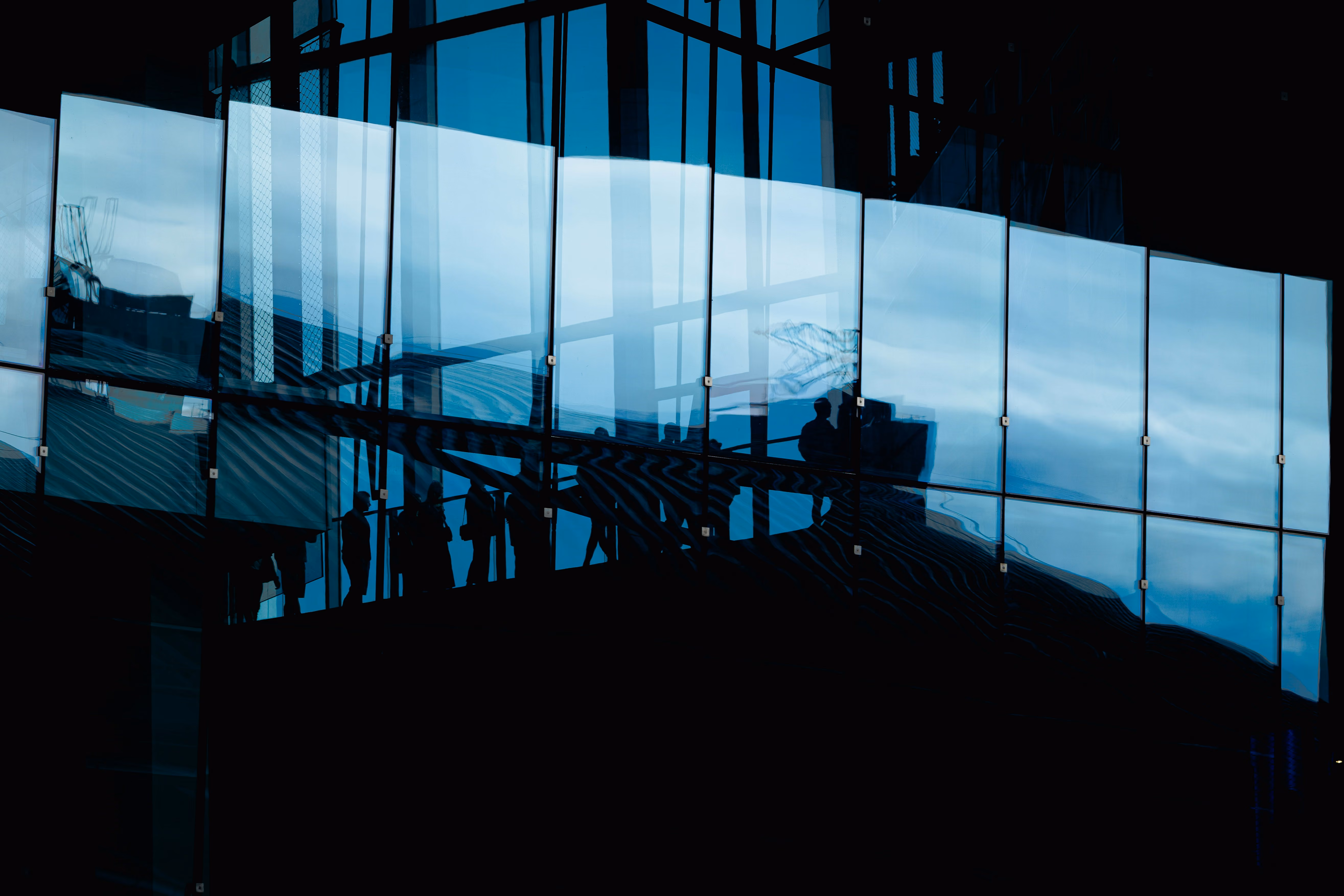 Silhouettes of people walking behind a glass office building facade