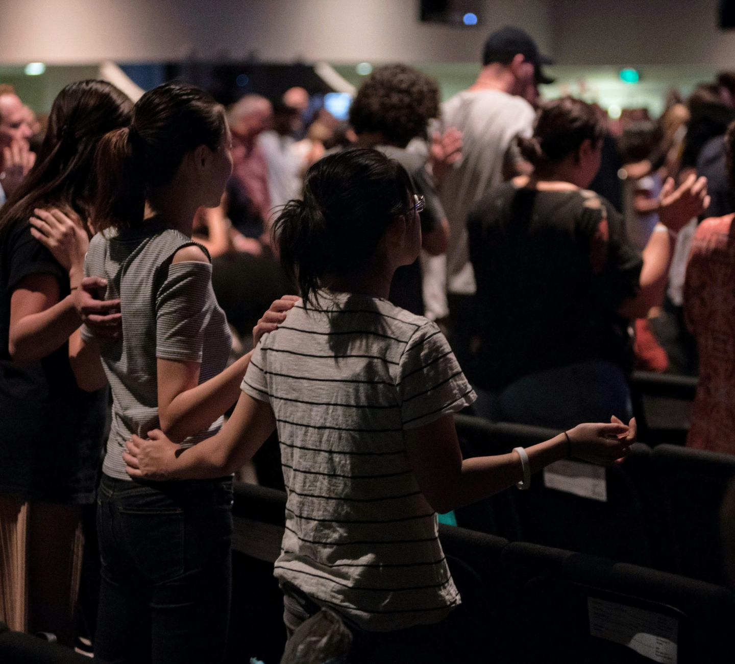 Group of people standing closely with arms around each other in a dimly lit room.