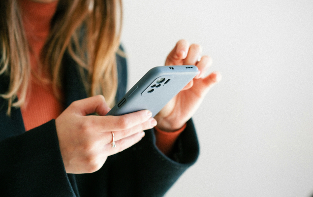 Person holding and using a smartphone with both hands against a plain light background.
