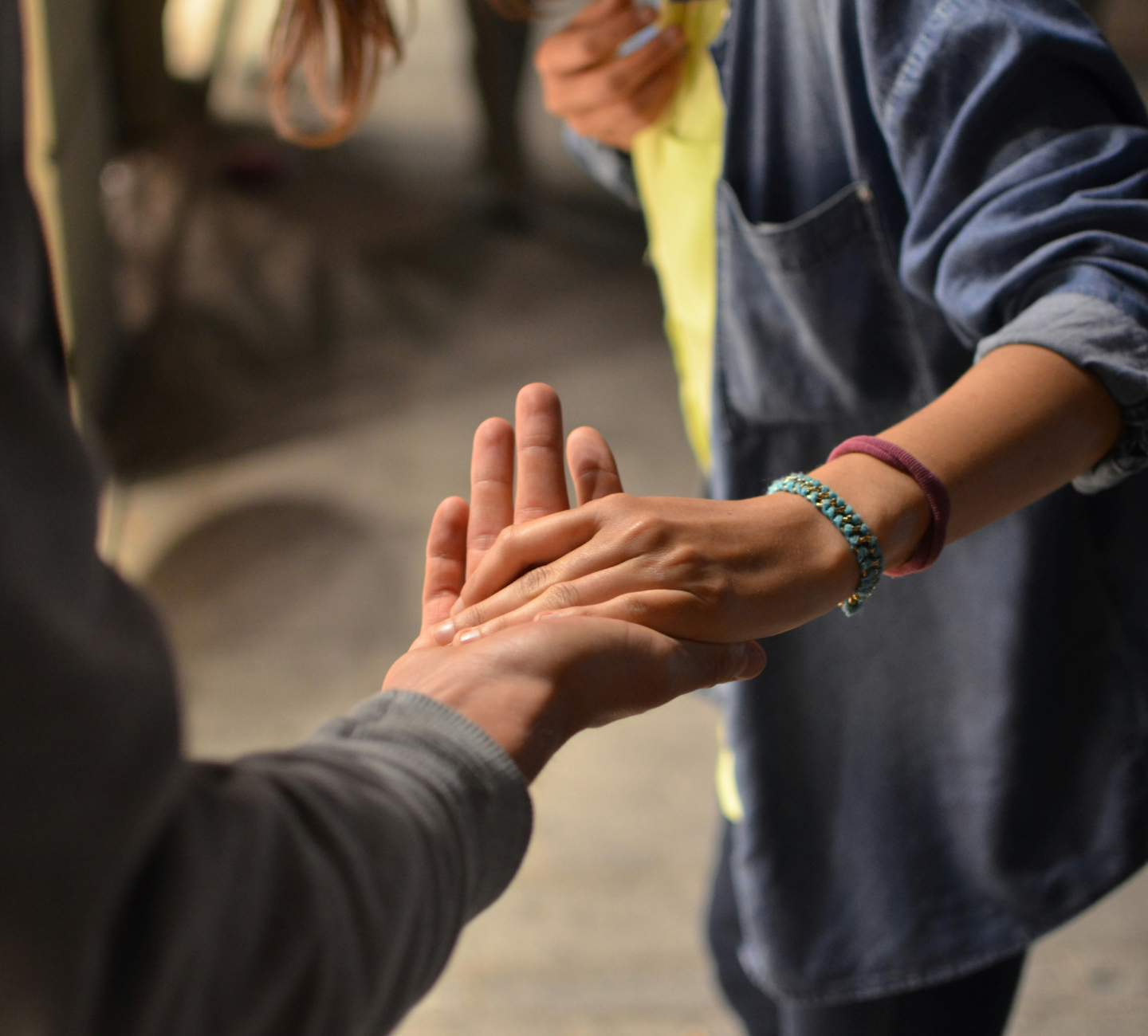 Two people touching hands in a supportive gesture, one wearing a beaded bracelet and hair tie.