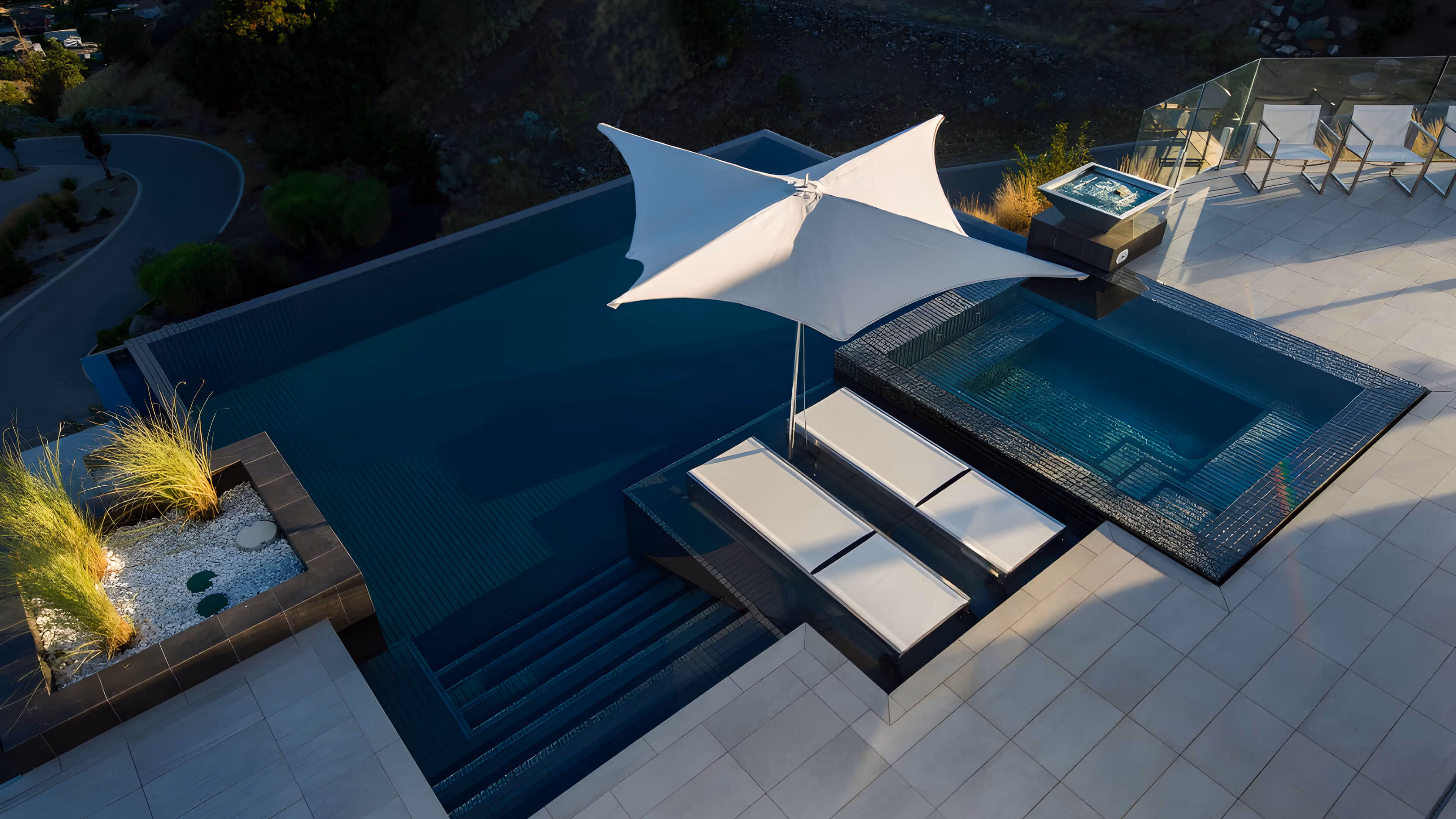 Modern outdoor pool area with built-in lounge beds under a large white umbrella and a small raised hot tub on a tiled patio.