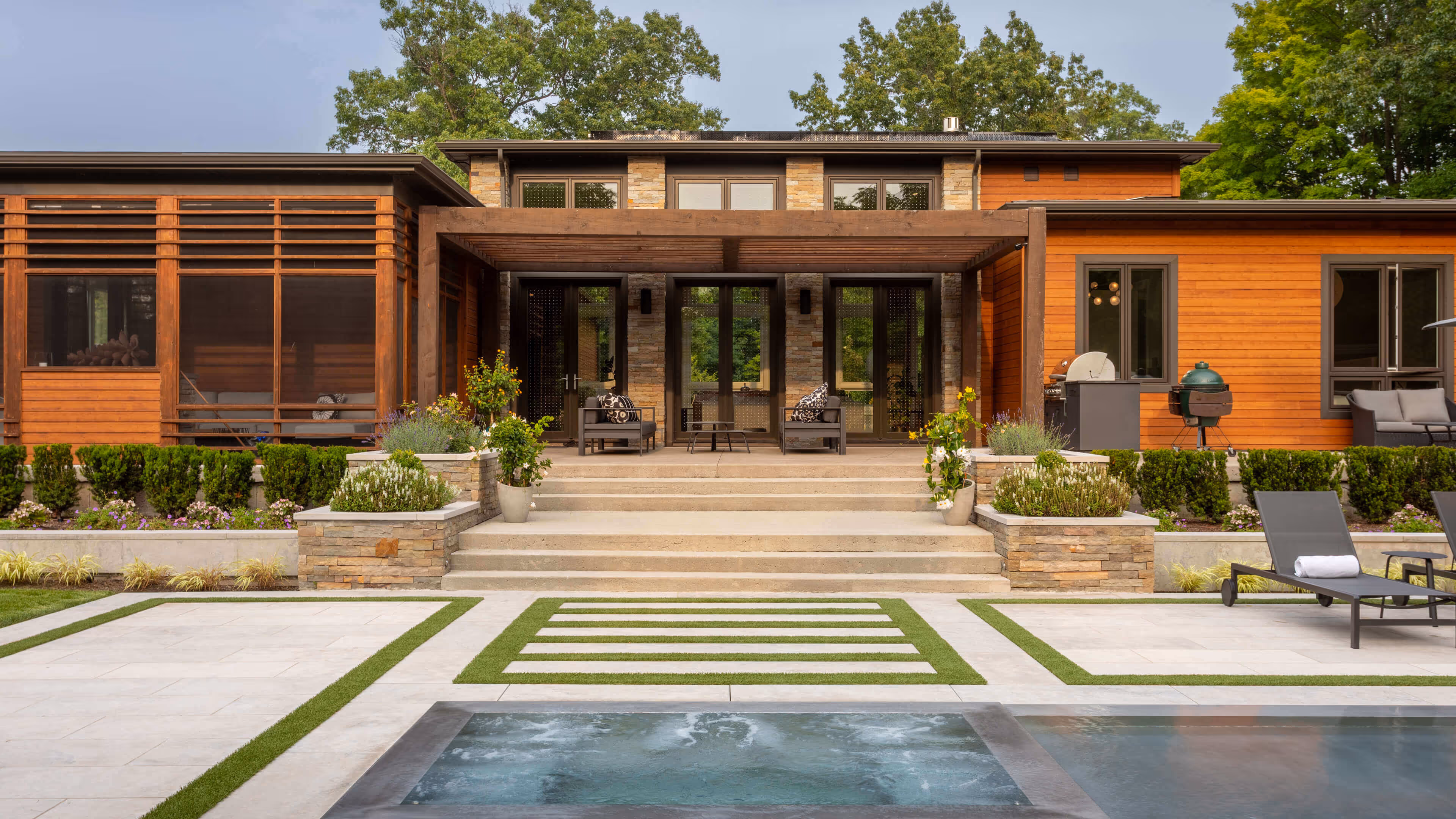 Modern wooden house with a stone terrace, patio furniture, and a pool in the foreground.