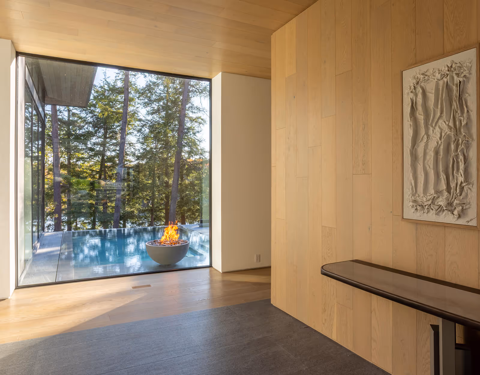 Modern room with large window showing outdoor pool, fire pit, and trees beyond.