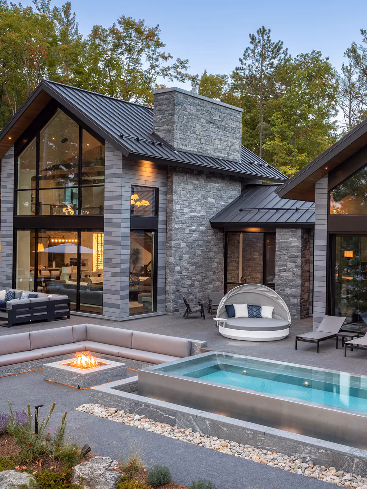 Modern house with large glass windows, outdoor fire pit seating, a pool, and patio furniture.