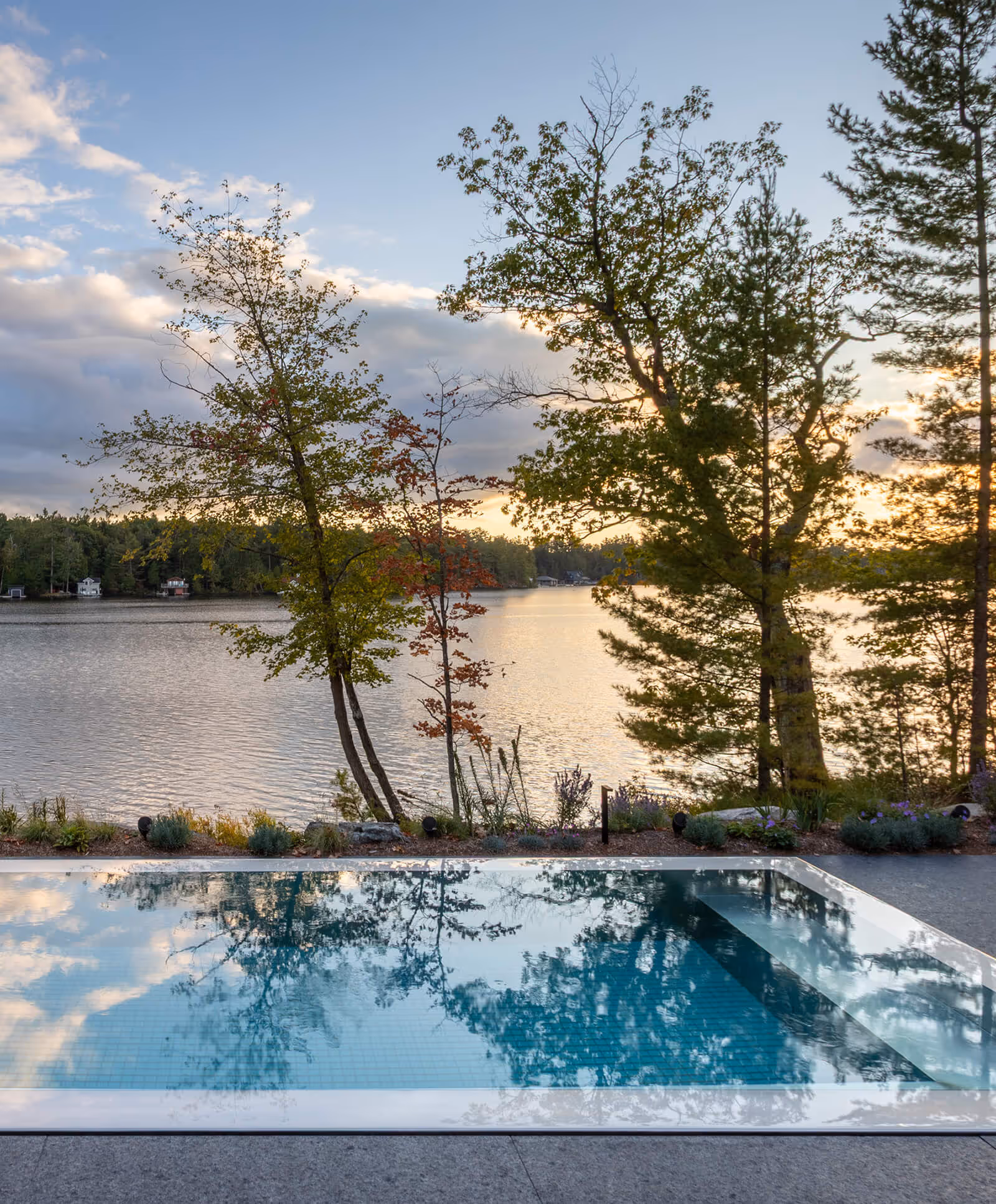 Pool reflecting trees beside a lake at sunset with partly cloudy sky and forested shoreline.