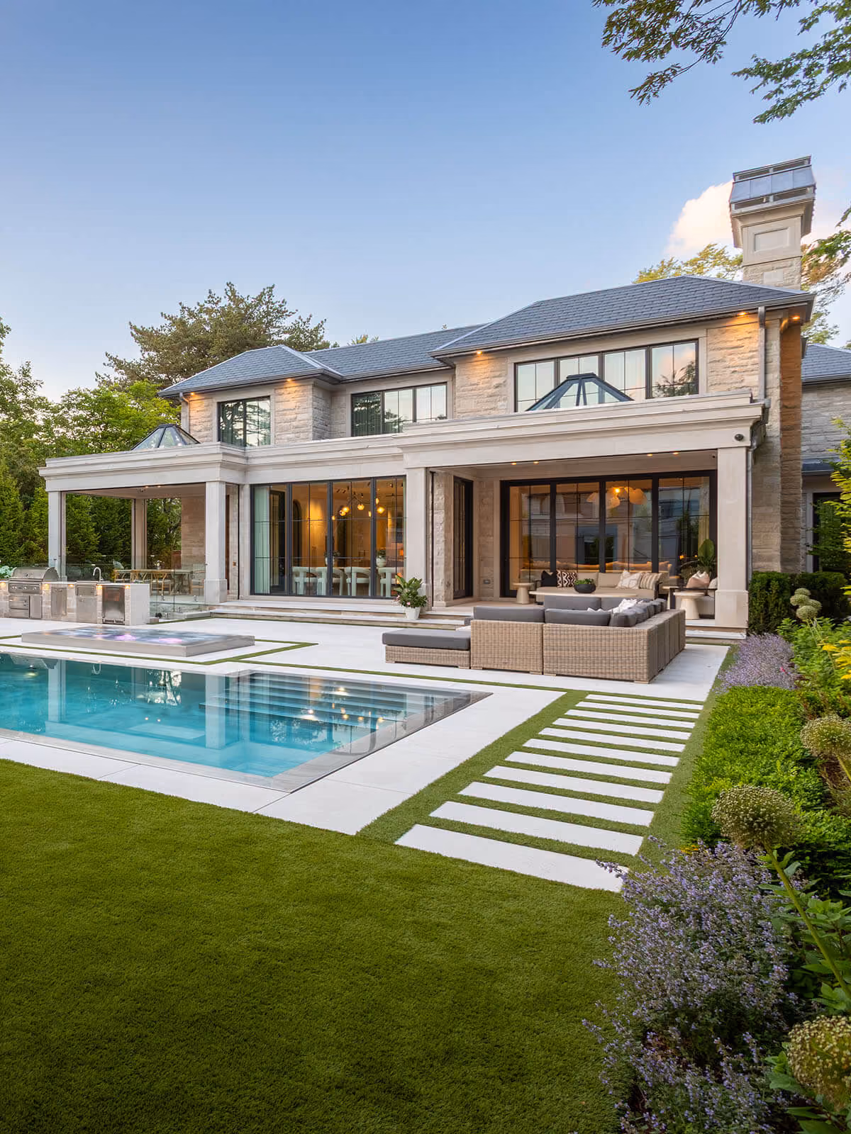 Modern house with a pool, outdoor sofa, and green lawn with pathway in the backyard.